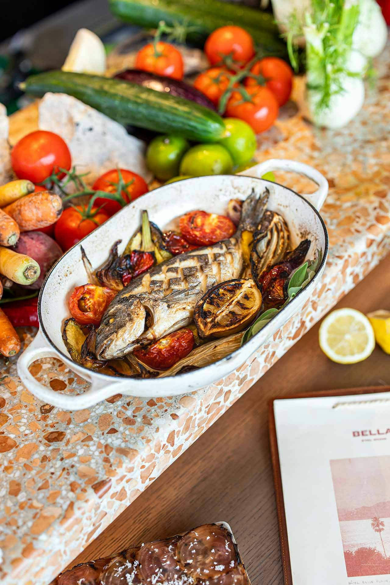 Fresh grilled fish on a bed of blistered, roast tomatoes and lemon on a pink terrazzo bench