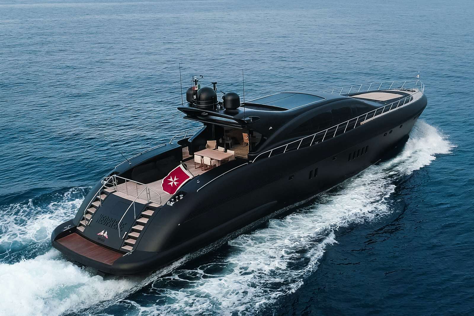 A sleek black Mangusta 108 yacht cruising on the ocean, its deck featuring an outdoor lounge and dining area.