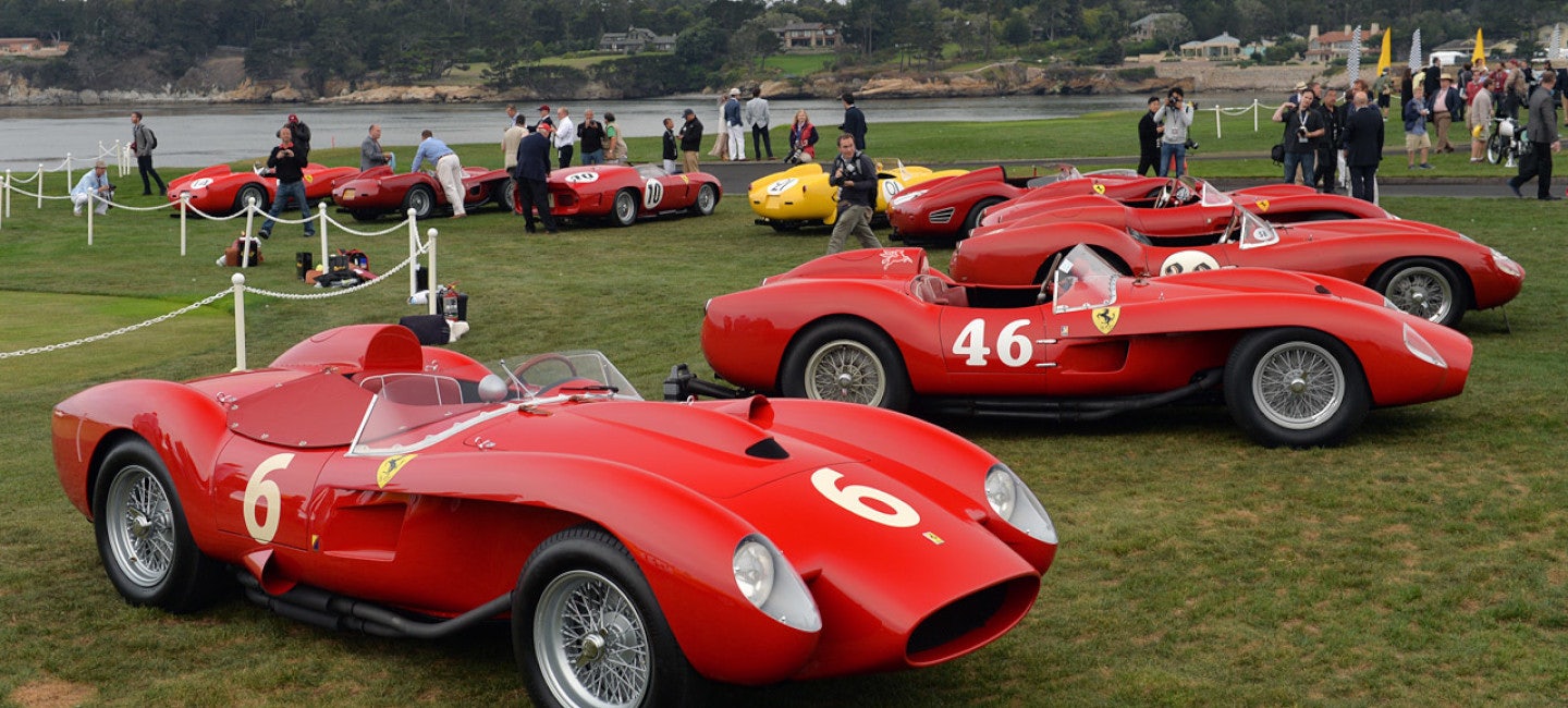 A mesmerizing scene featuring a collection of stunning Ferraris and classic cars on a coastal grassland. Enthusiastic car lovers admire these automotive treasures on a cloudy day during the Pebble Beach Concours d'Elegance, a highlight of the Pebble Beach Automotive Week.