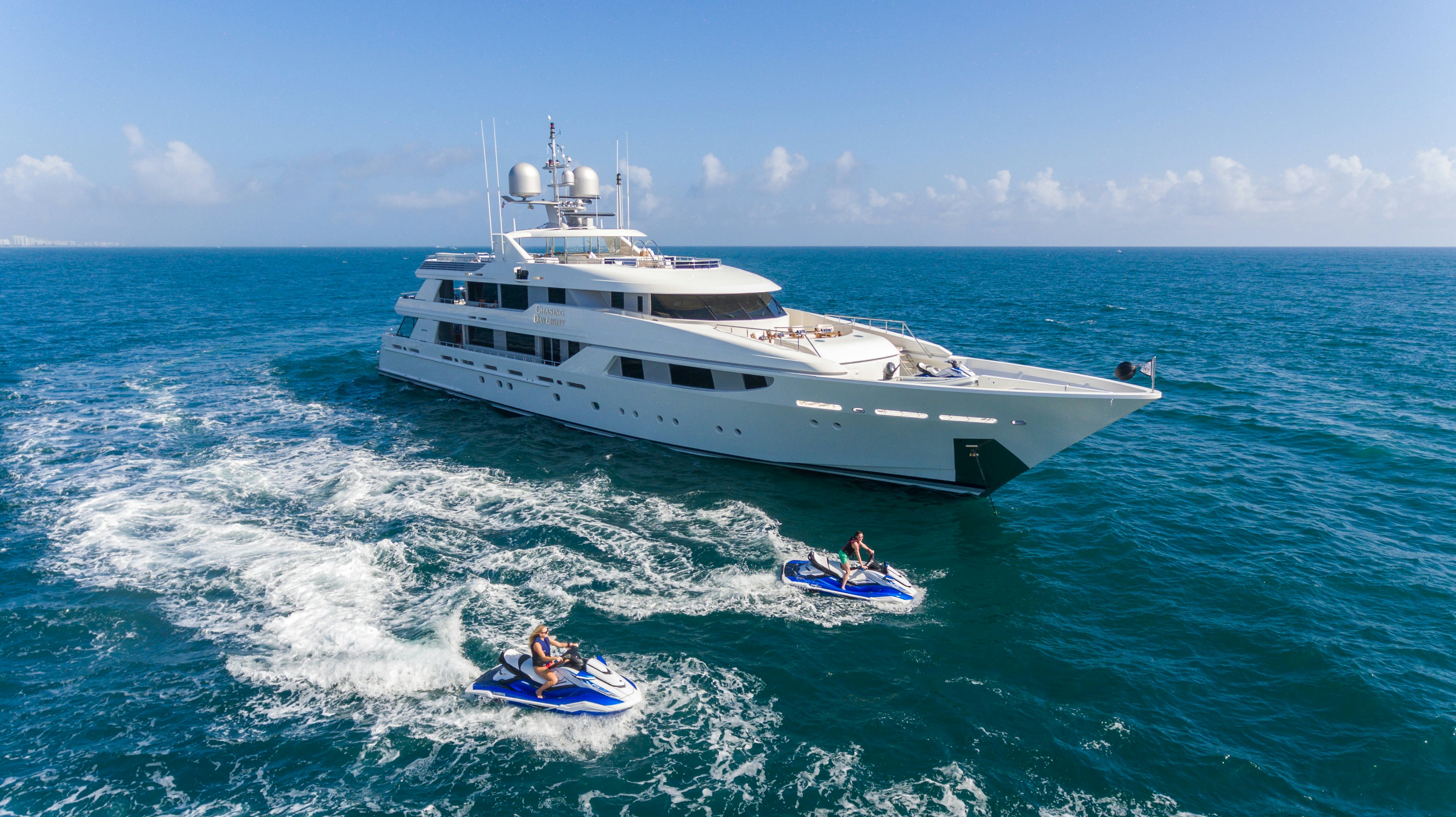 CHASING DAYLIGHT white yacht cruising in the blue ocean with jet skis to her left