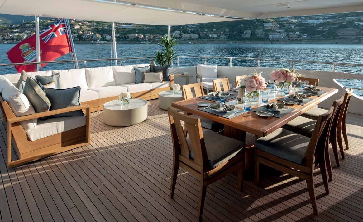 Alfresco dining setup on a Heesen 55 Steel yacht's deck, with coastal views, showcased by Northrop & Johnson.
