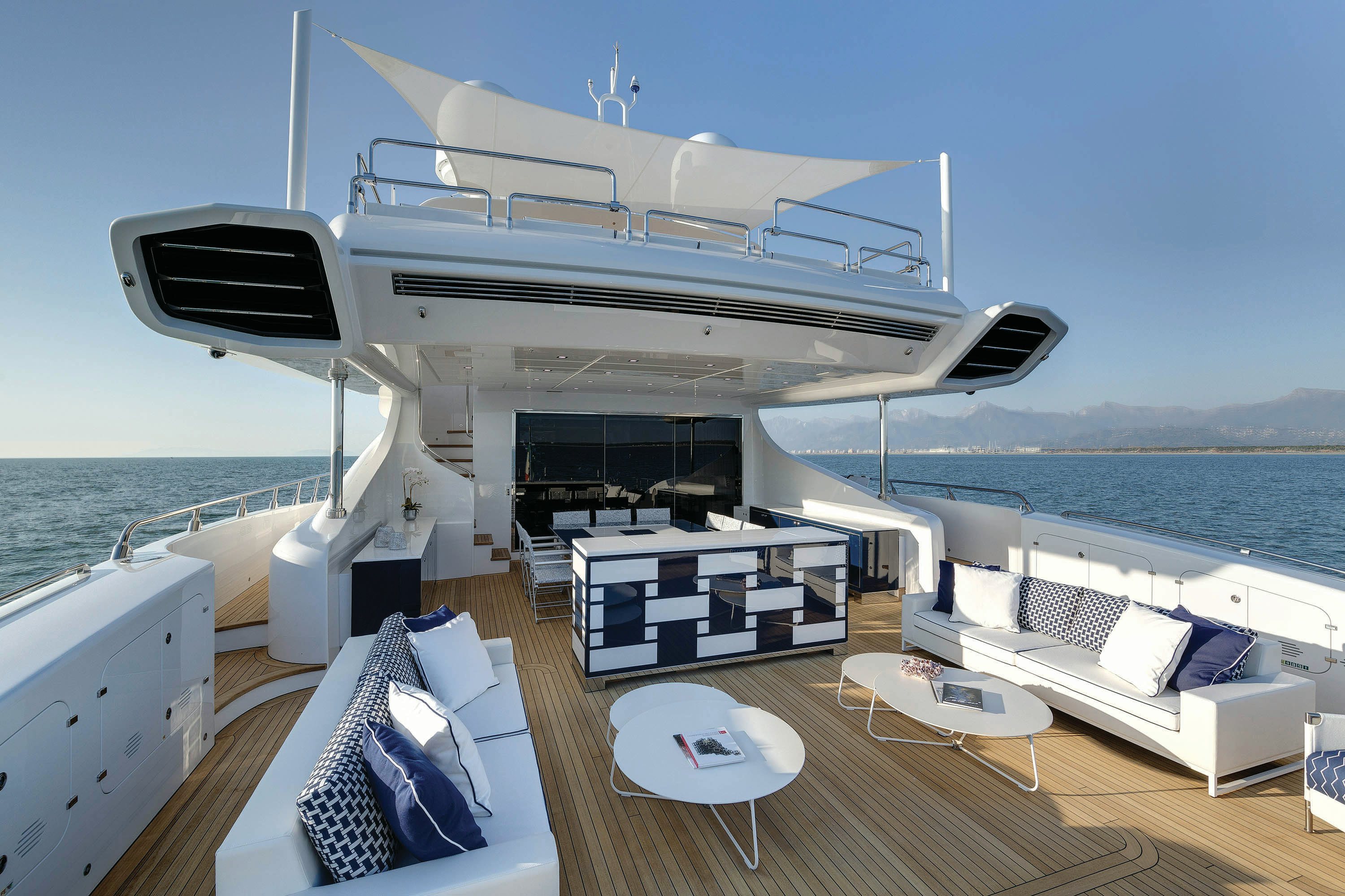 Open Air Elegance: The Mangusta 165 Deck A pristine outdoor lounge area on the Mangusta 165 yacht, with modern white and blue furnishings, against a backdrop of calm seas and clear skies.
