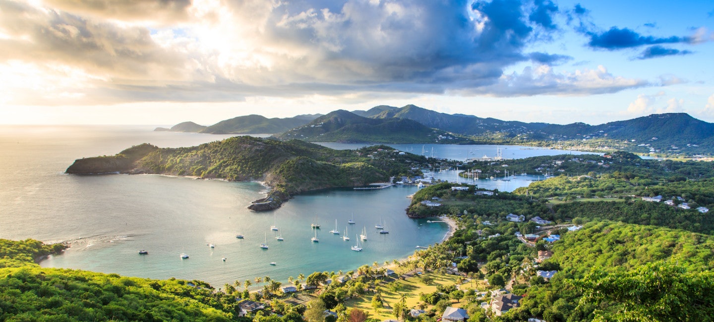 A stunning view of Antigua's landscape featuring lush green hills, a deep blue sea, and dramatic clouds, captured during the Superyacht Challenge Antigua.