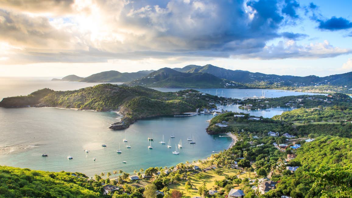 A stunning view of Antigua's landscape featuring lush green hills, a deep blue sea, and dramatic clouds, captured during the Superyacht Challenge Antigua.