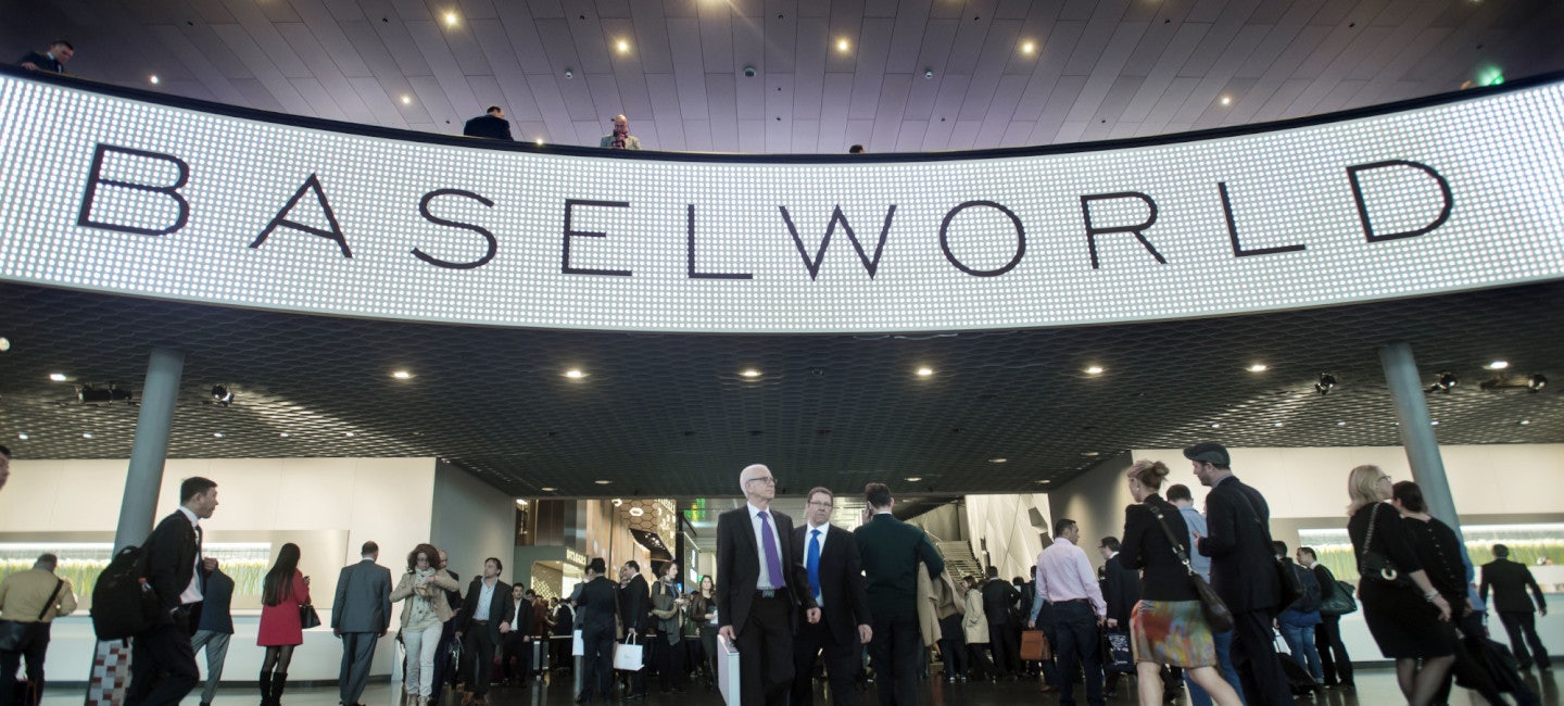A bustling scene at the entrance of Baselworld, with a crowd of well-dressed individuals eagerly awaiting the commencement of the event.