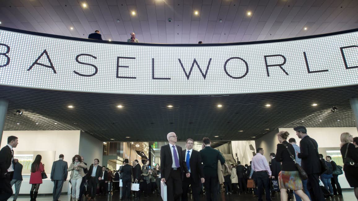 A bustling scene at the entrance of Baselworld, with a crowd of well-dressed individuals eagerly awaiting the commencement of the event.
