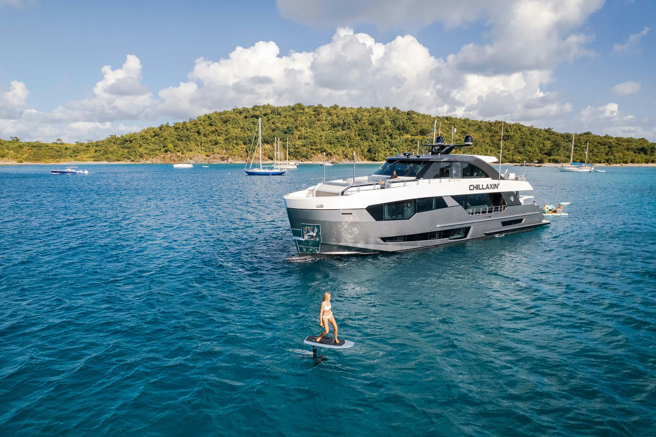 Charter yacht for 6 to 8 guests at anchor with woman cruising the blue waters on hydrofoil board