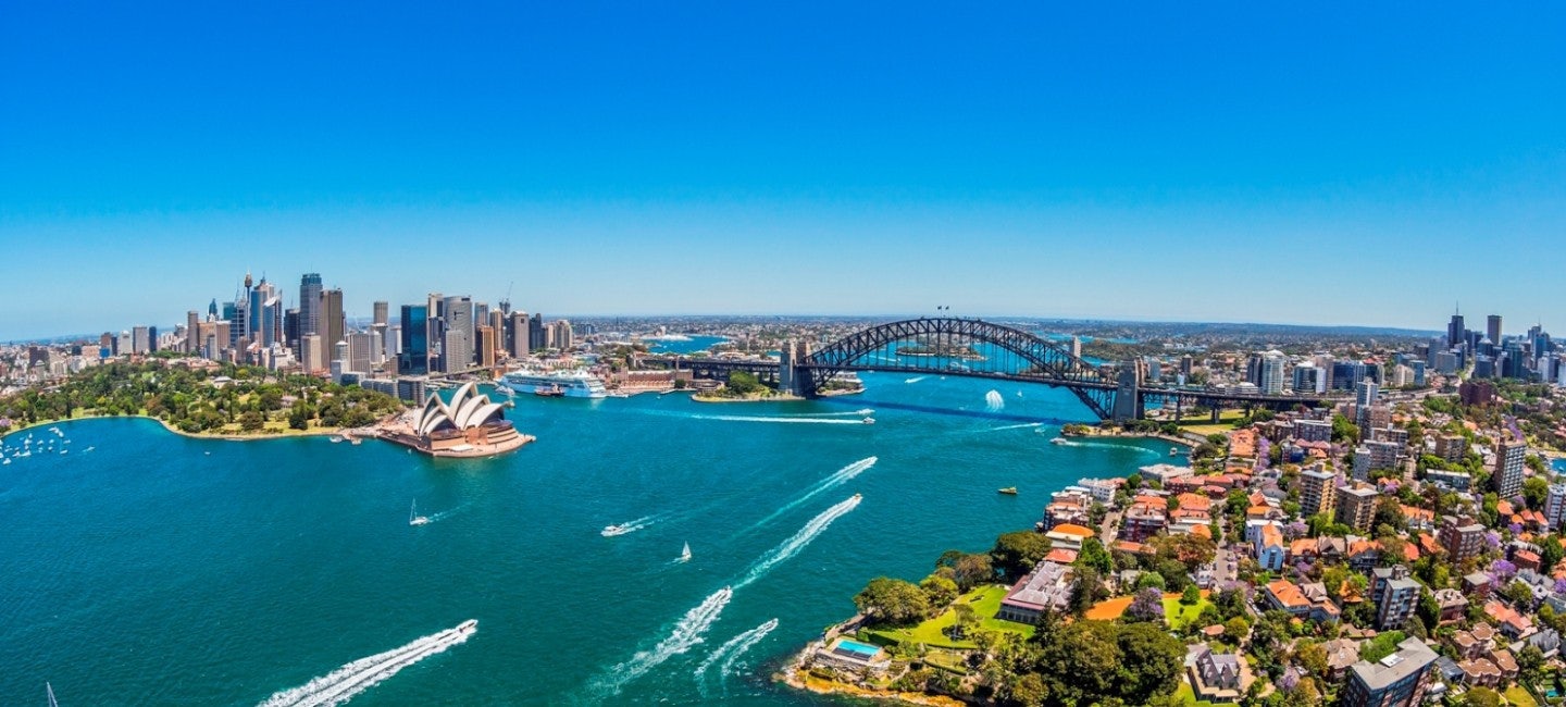 A breathtaking aerial view of Sydney Harbor Bridge against a backdrop of azure skies and the tranquil blue sea. Boats cruise beneath the iconic bridge during the Sydney International Boat Show.