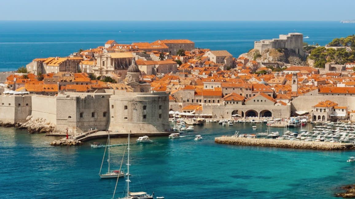 An enchanting aerial view of Dubrovnik's historic old village and picturesque port under the radiant sun during the Dubrovnik Summer Festival.