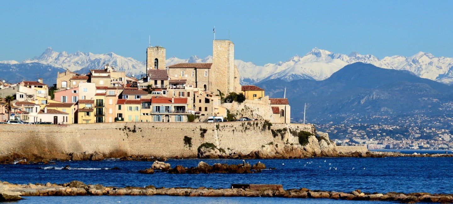 A picturesque side view of the historic Antibes Old Village against the backdrop of the sparkling sea on a sunny and wavy day.