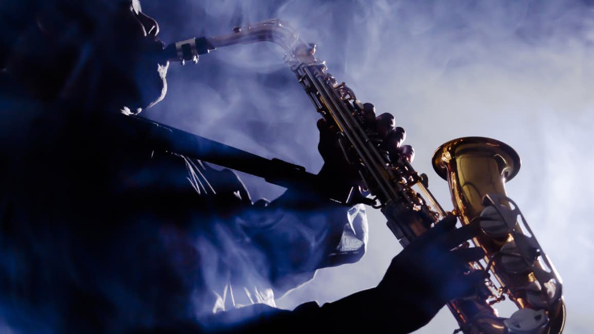 A skilled saxophonist playing passionately in the dimly lit night, enveloped by a mystical fog at the renowned Nice Jazz Festival. To fully enjoy this event, consider chartering an N&J yacht, the ultimate way to experience the festival's magic and music.