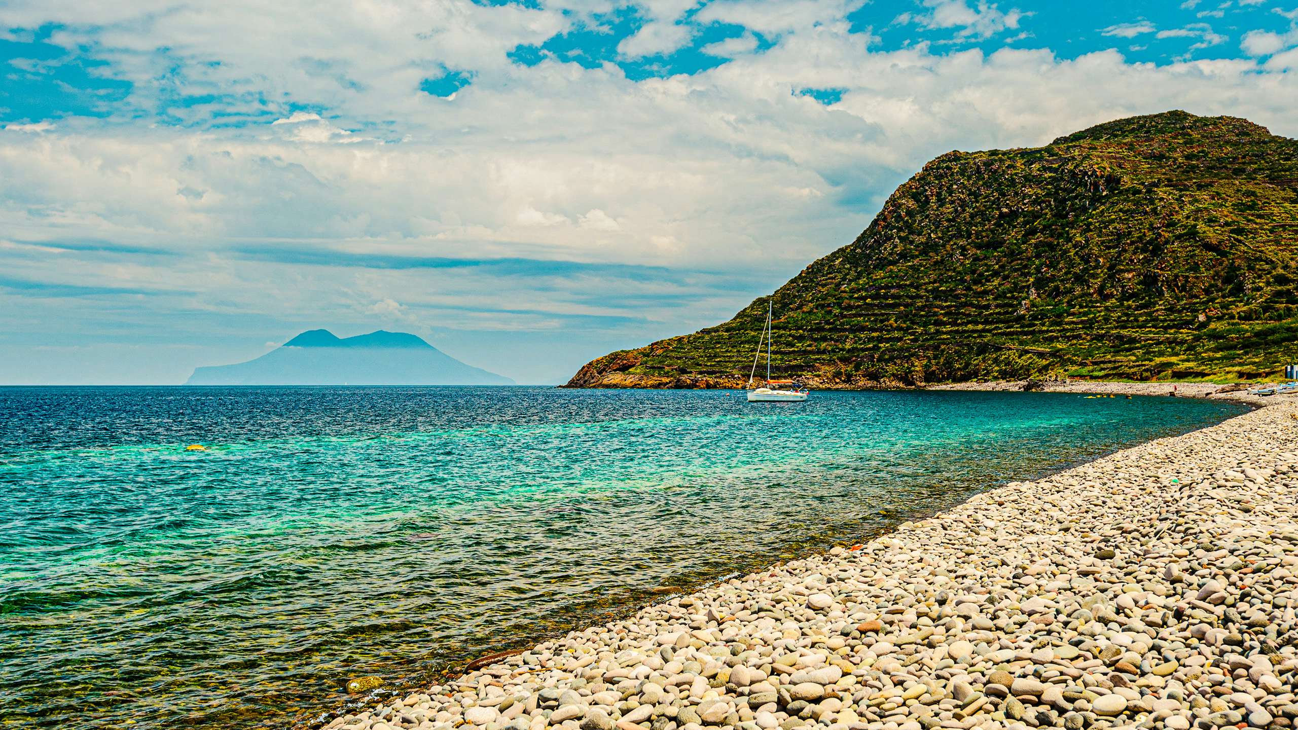 A serene pebbled beach in Sicily with crystal-clear waters, accessible via a luxury yacht charter with N&J.