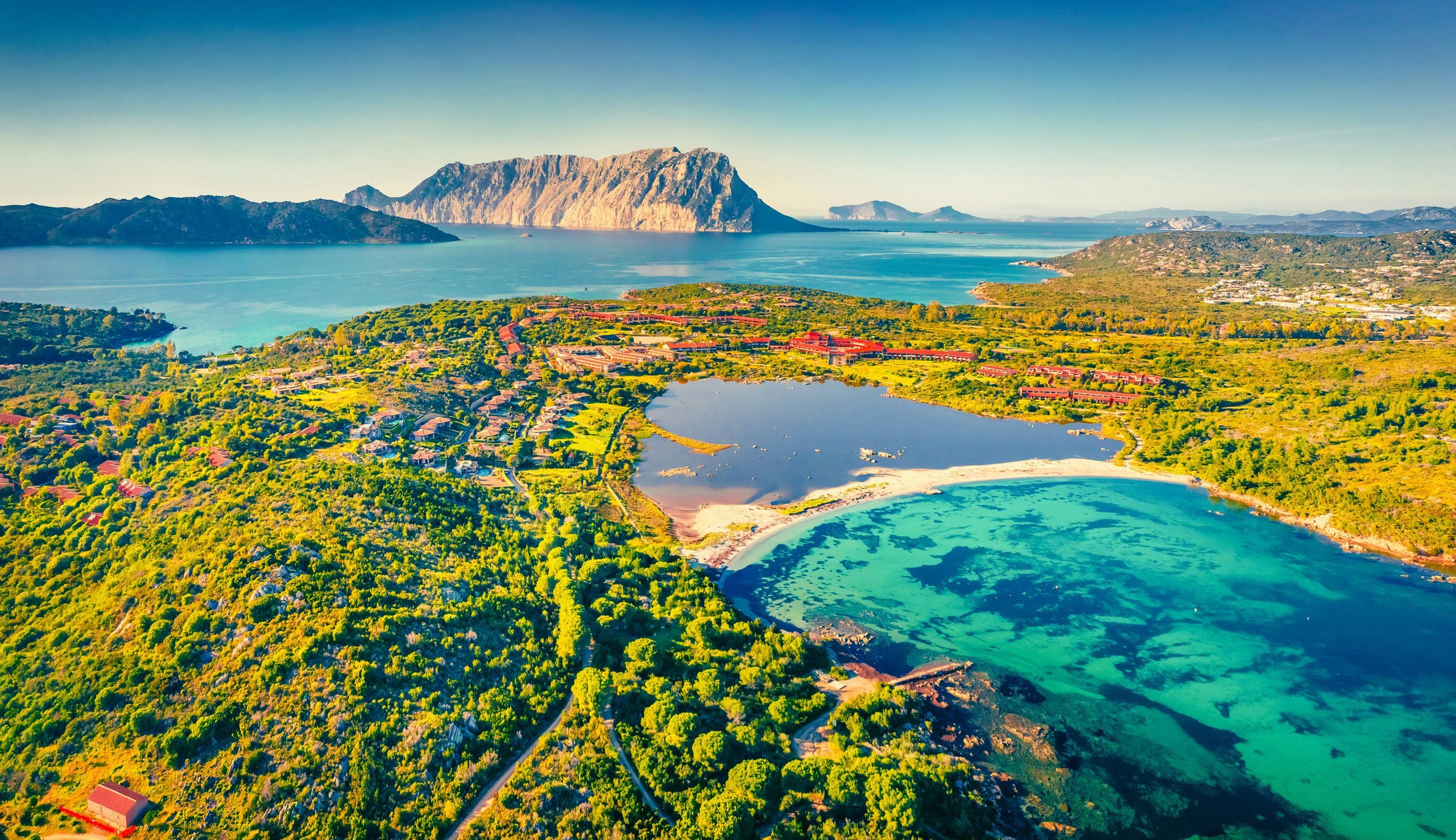 Aeolian Adventure Awaits - Set Sail with Northrop & Johnson Aerial view of a lush Aeolian island with vivid blue waters and rugged mountains in the distance.
