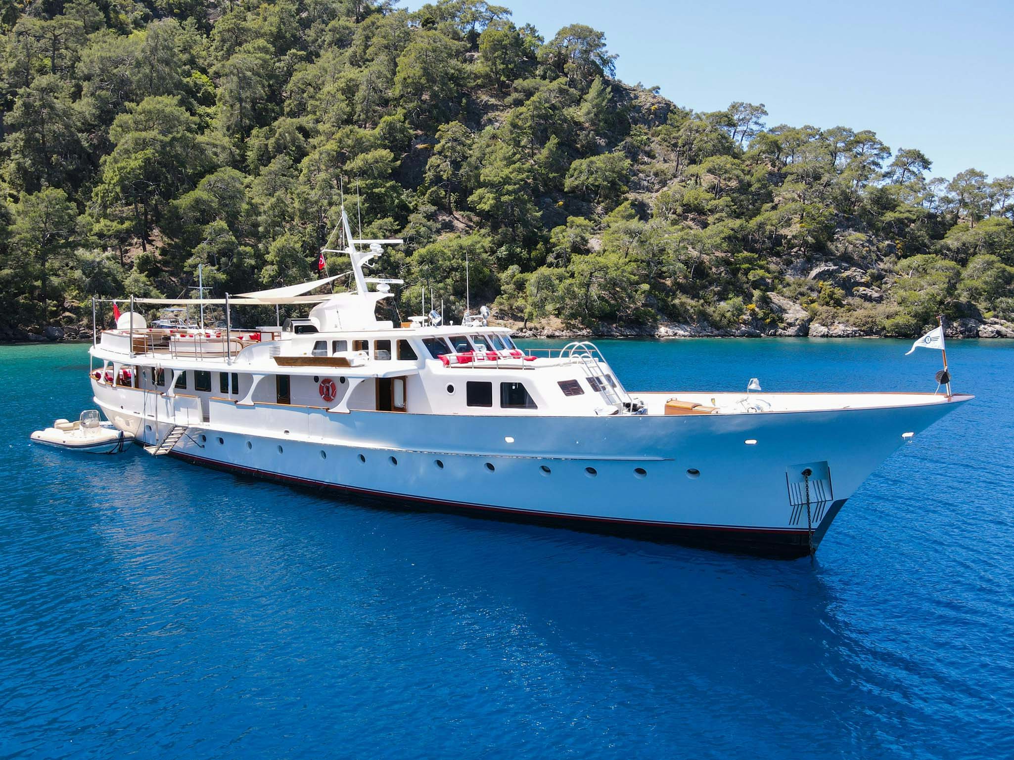 motor yacht alhambra anchored i nthe blue ocean in front of green trees ashore