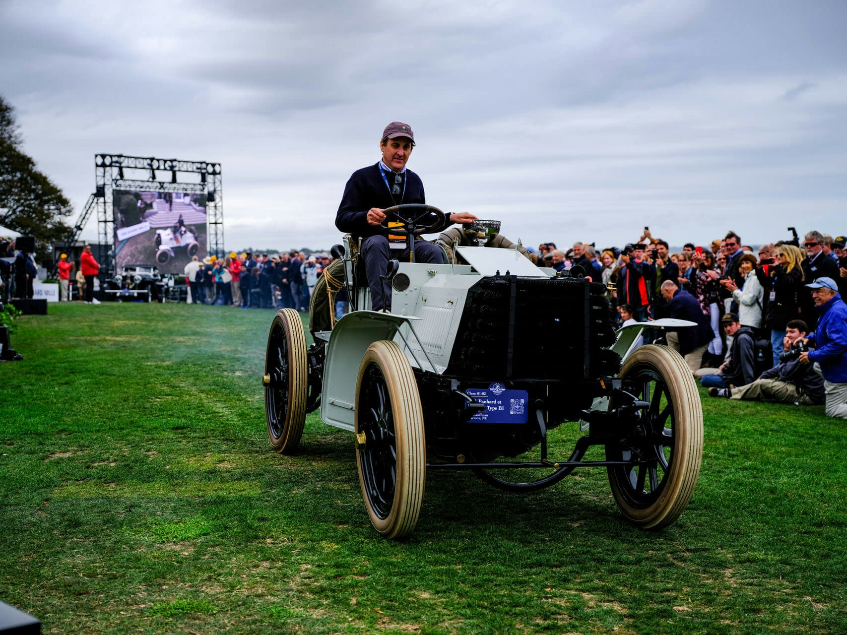 Man driving a classic car in a parade at Audrain&#039;s Newport Concours Motor Week