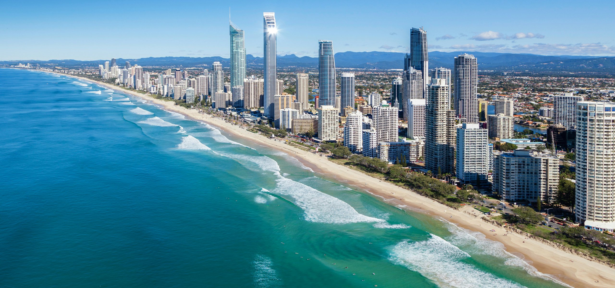 Aerial view of a bustling Australian city skyline adjacent to a golden beach.