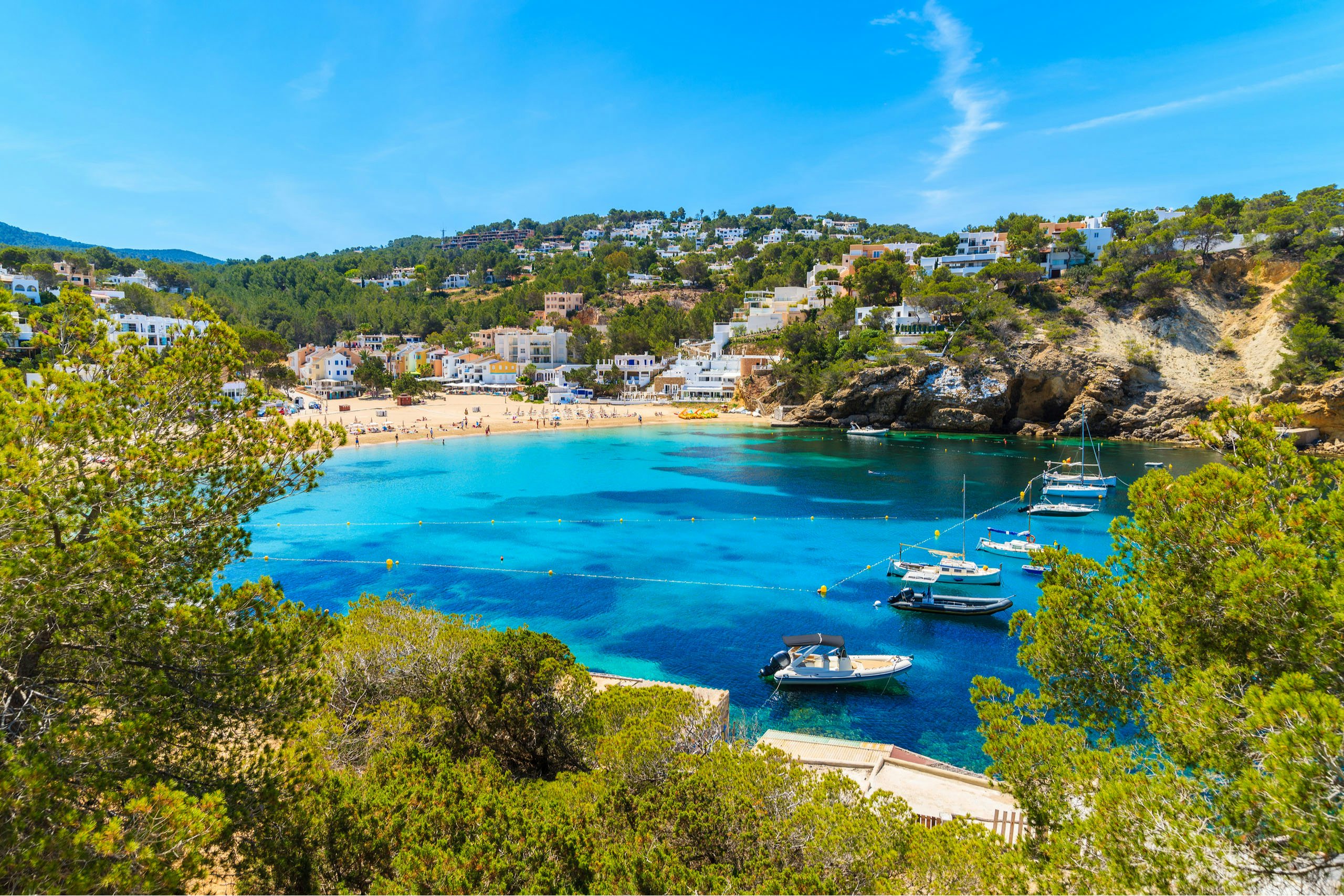 Cala Vadella's Tranquil Cove | Balearic Islands Sailing | Northrop & Johnson Yachts anchored in the tranquil azure waters of Cala Vadella, embraced by the lush green landscape.