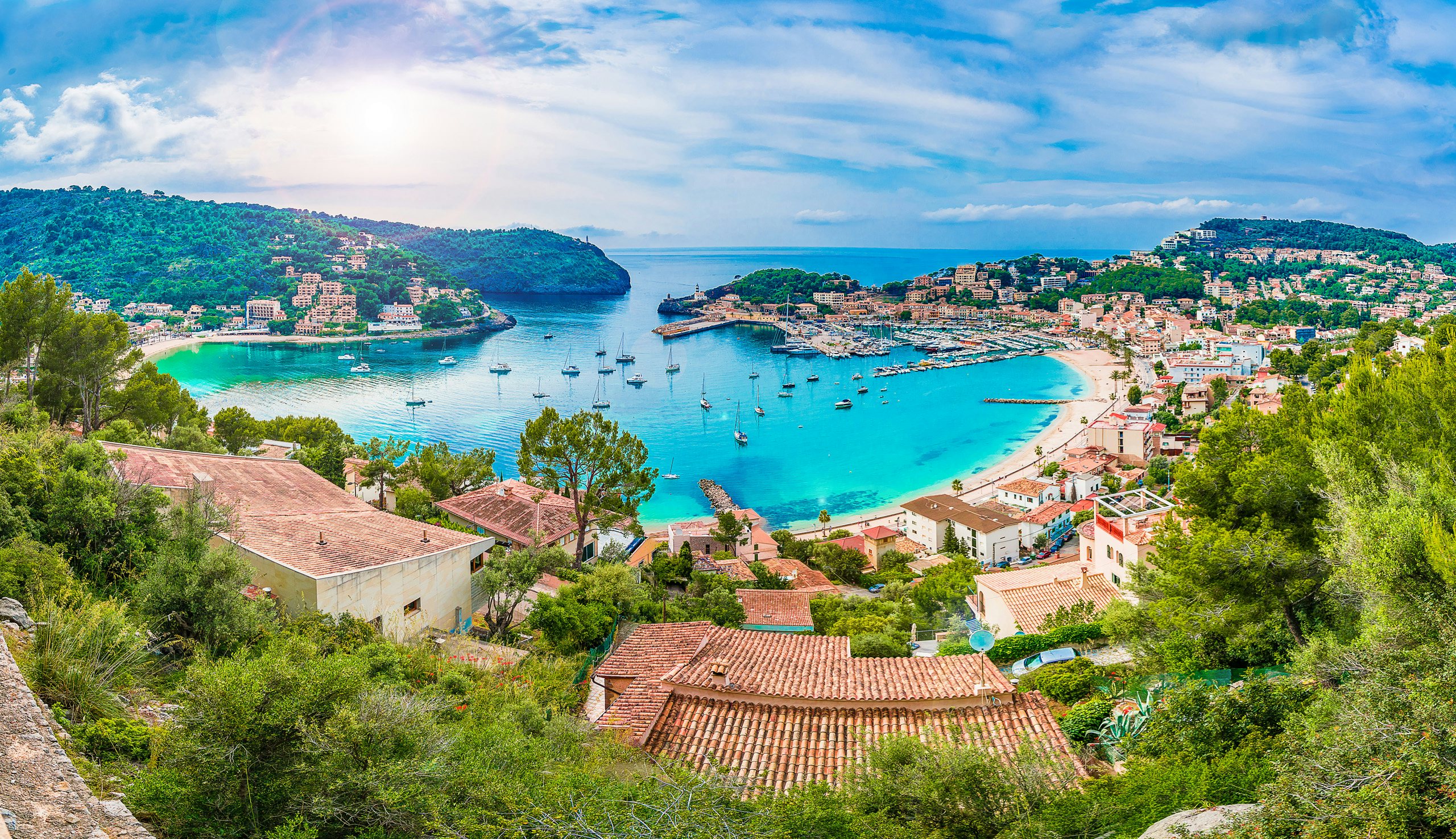 Overlooking the picturesque bay of Soller with its clear waters and bustling beachfront under a bright sky.