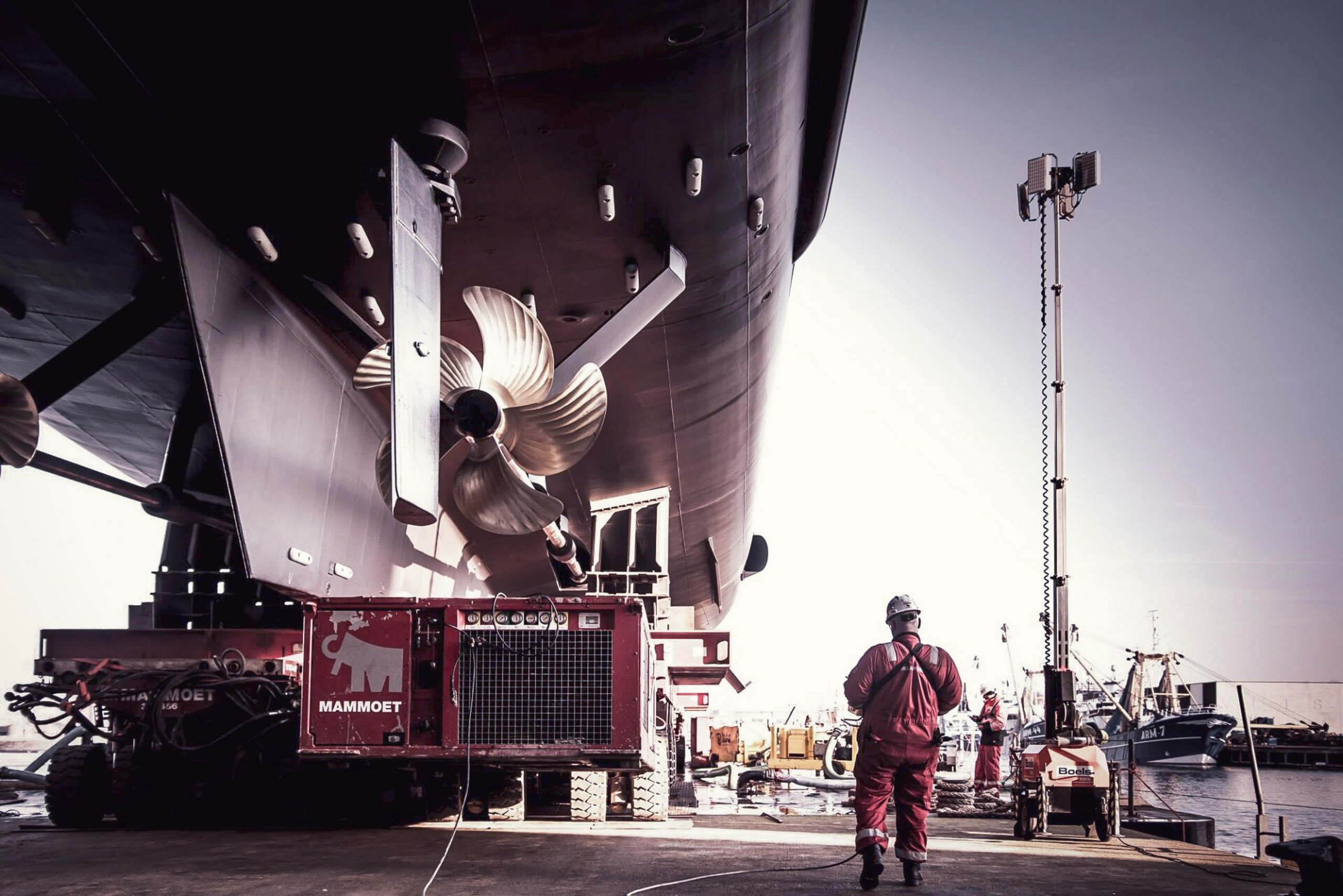 Yacht at dry dock in a shipyard | Yacht for Sale | Northrop & Johnson Shipyard worker walking next to yacht at dry dock | Yacht for Sale | N&J