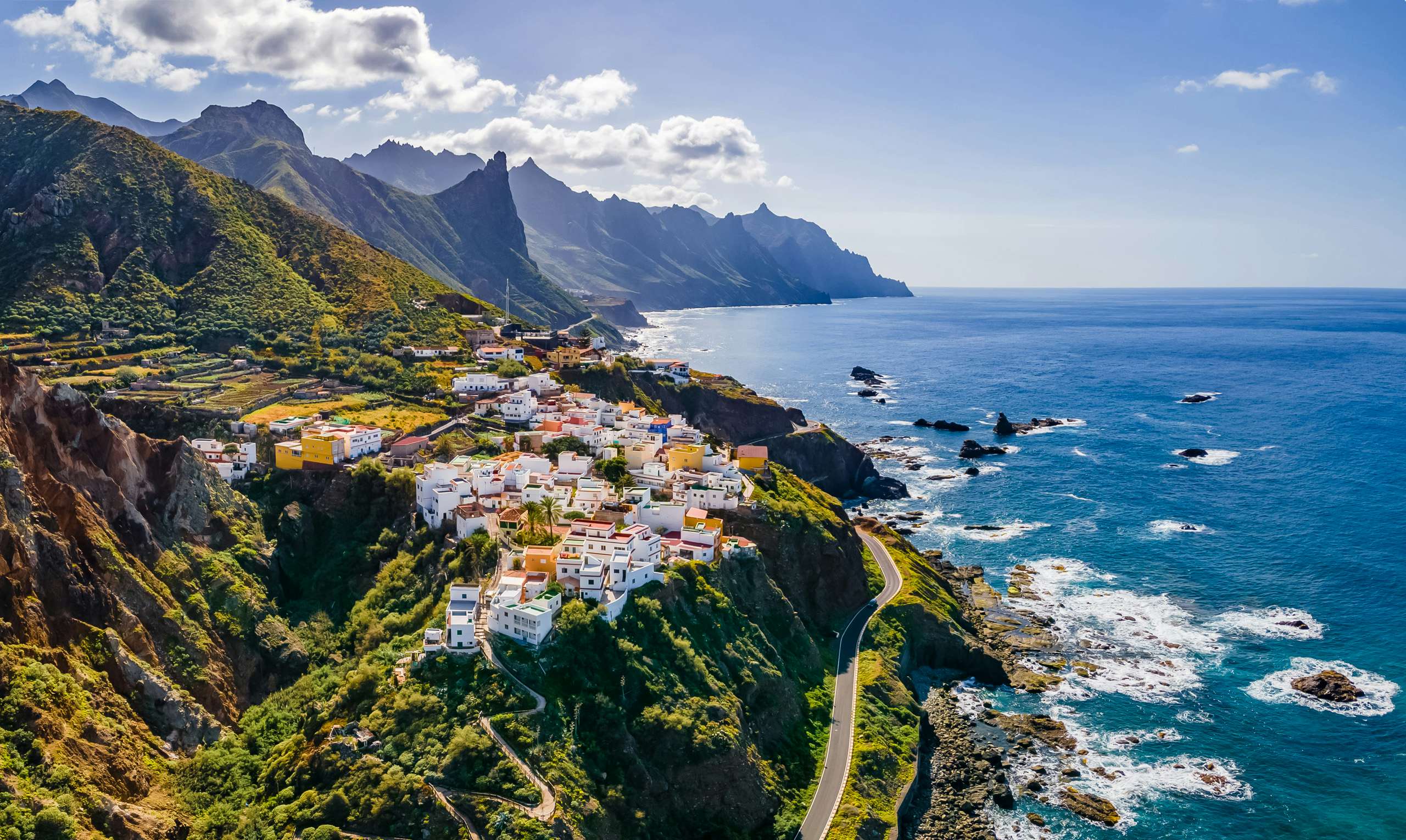 Sweeping aerial view of Tenerife's coastline showcasing a serene fishing village, inviting yachts to discover the Canary Islands' hidden treasures.