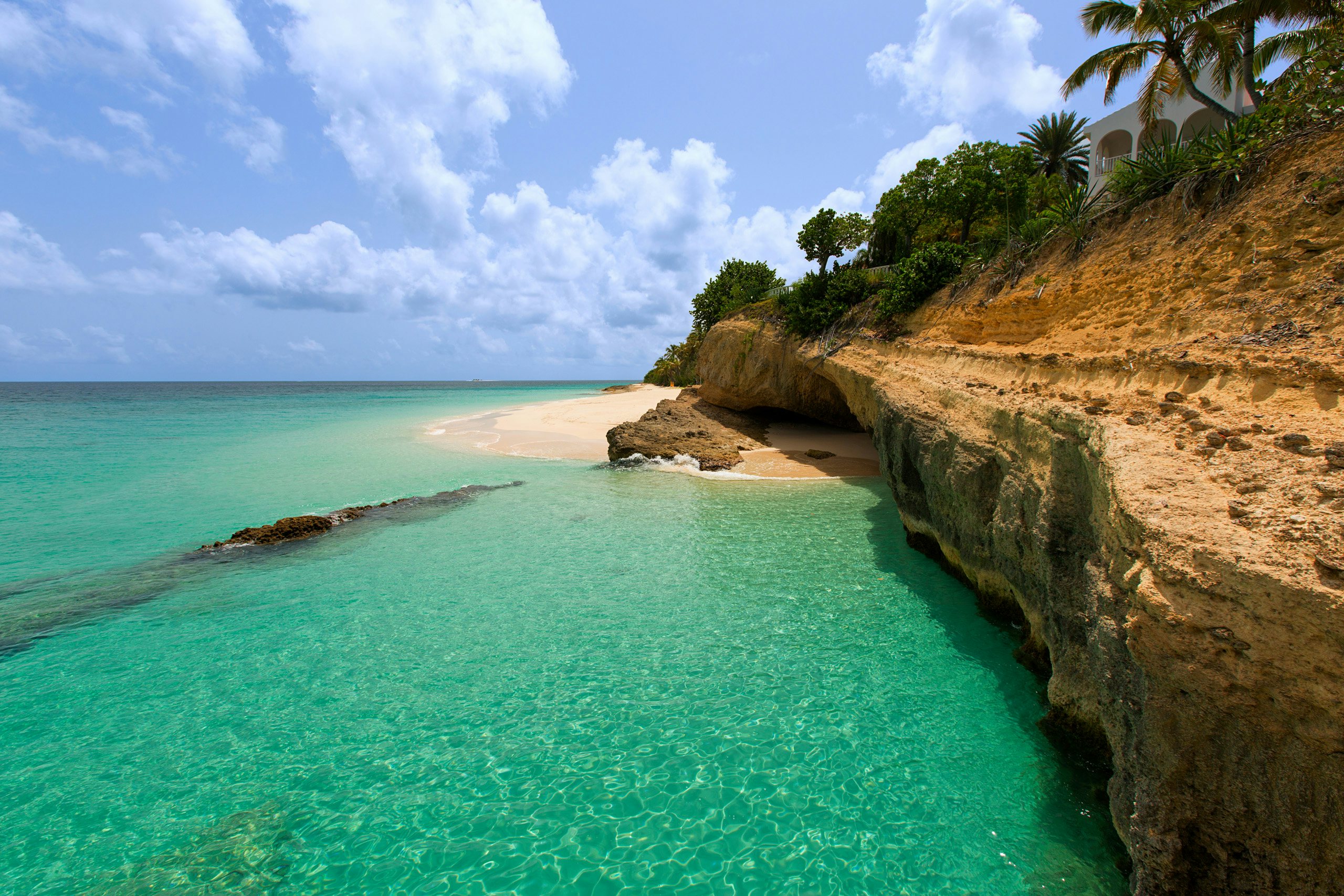 A breathtaking view of Anguilla's rugged rocky coast in the Caribbean, where turquoise waters meet a pristine white sand beach.