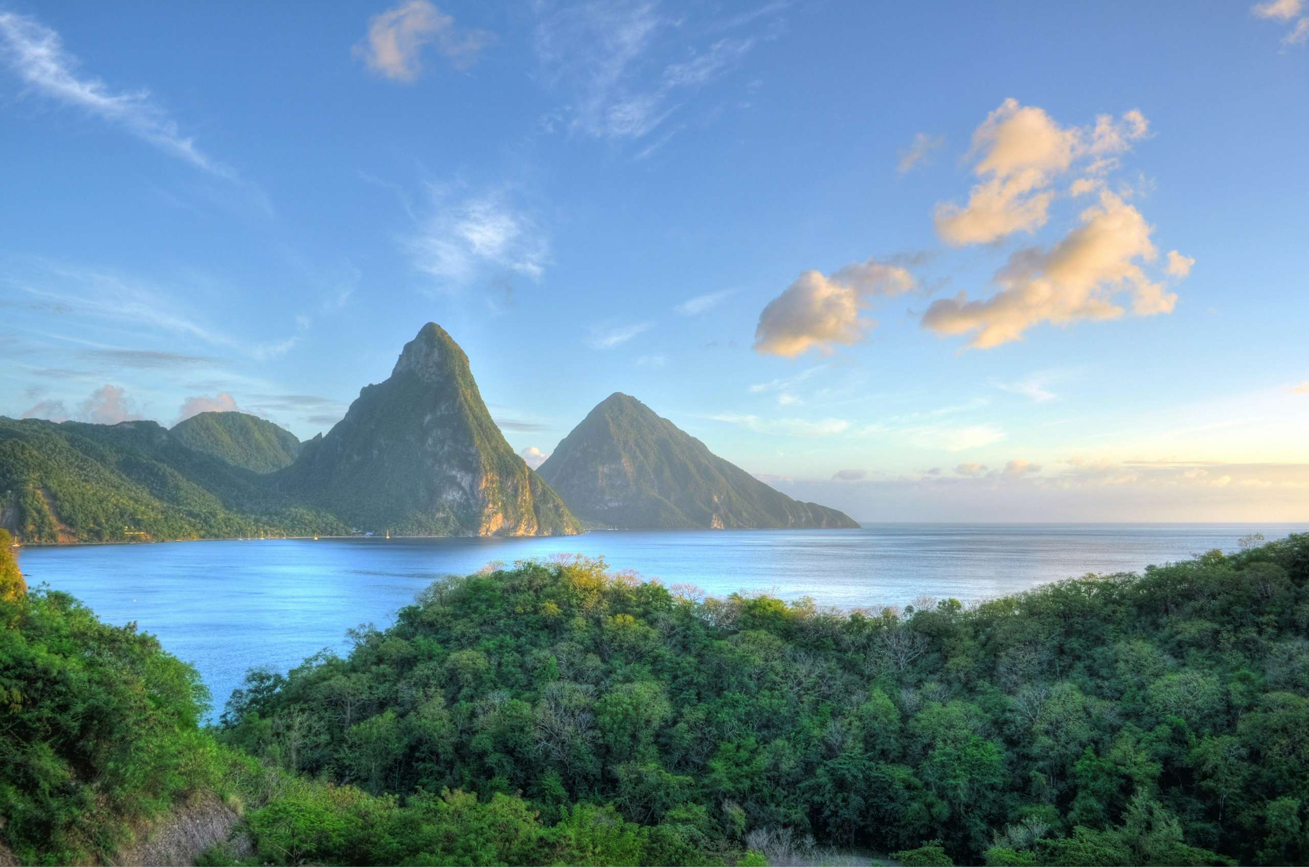 A serene daytime view of St. Lucia, featuring white sand beaches, untouched green nature, and foggy, high, pointed mountains in the background—a captivating scene for your Caribbean St. Lucia Charter Yacht journey.