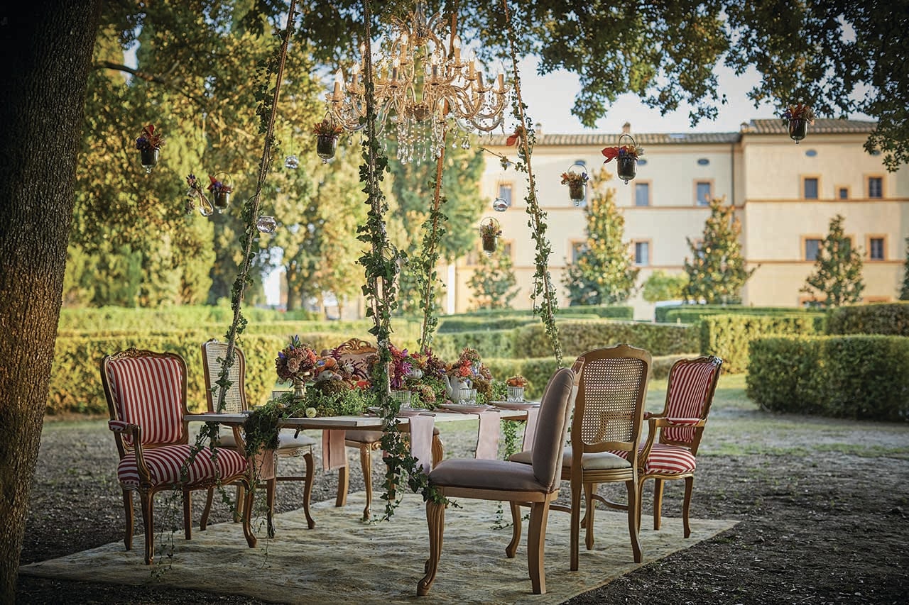 A wooden table and chairs surrounded by greenery in a garden of an old Italian castle