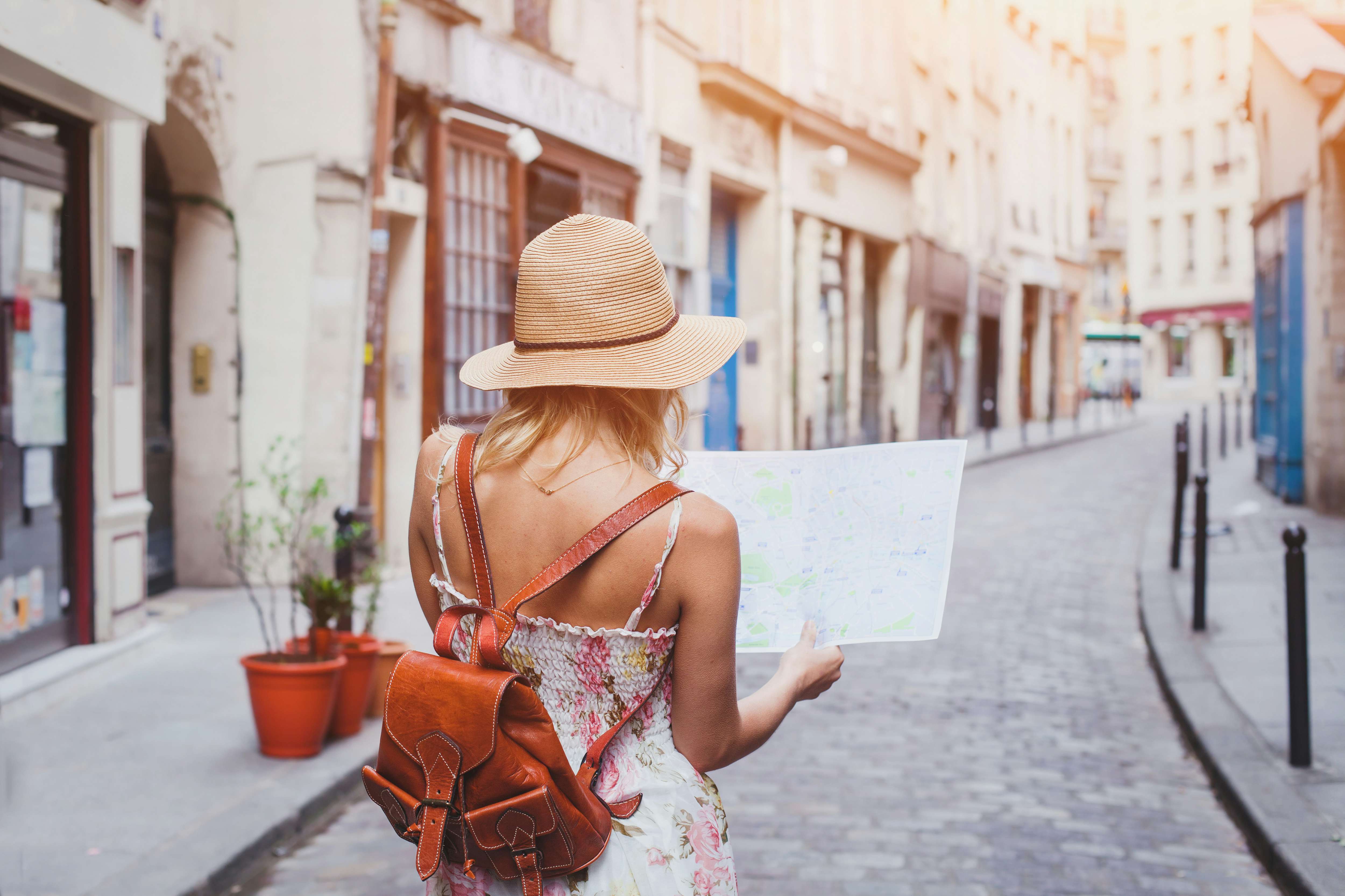 Back view of a woman in a summer dress and hat looking at a map on a quaint European street, symbolizing N&J's luxury European yacht charter services.