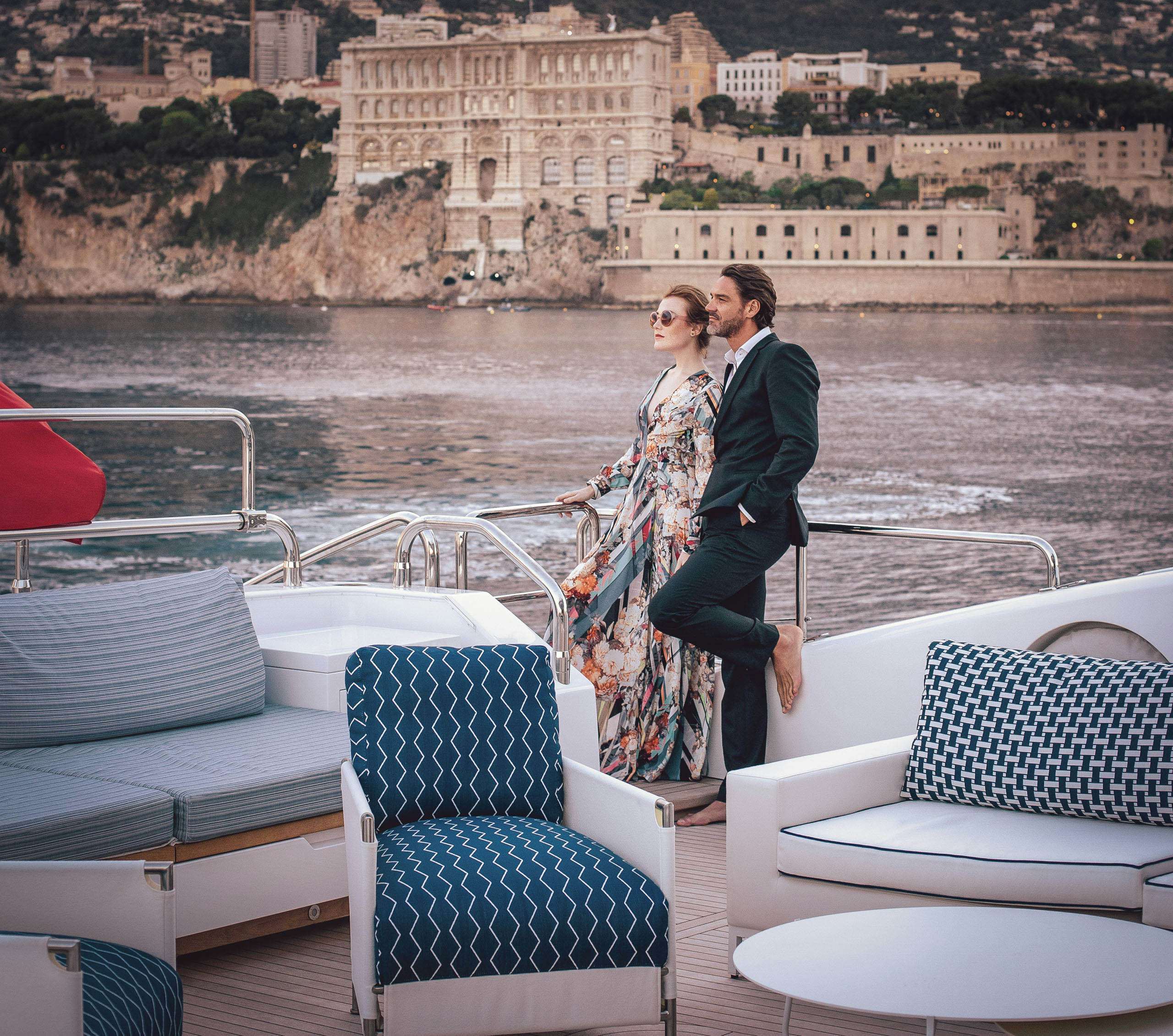 An elegant couple leans affectionately against the railing of a luxurious yacht, gazing out at the riviera coastline during the Cannes Film Festival.
