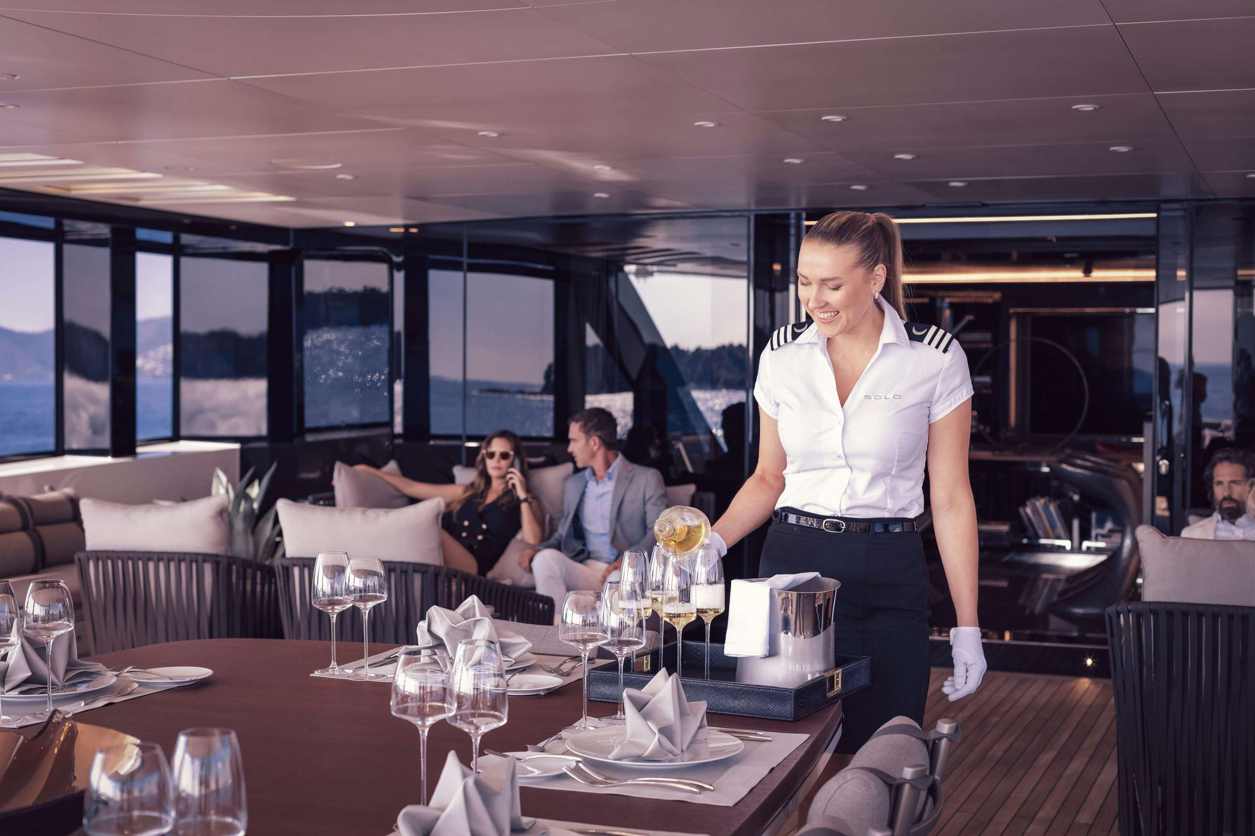 Stewardess serving champagne for couple on board charter yacht