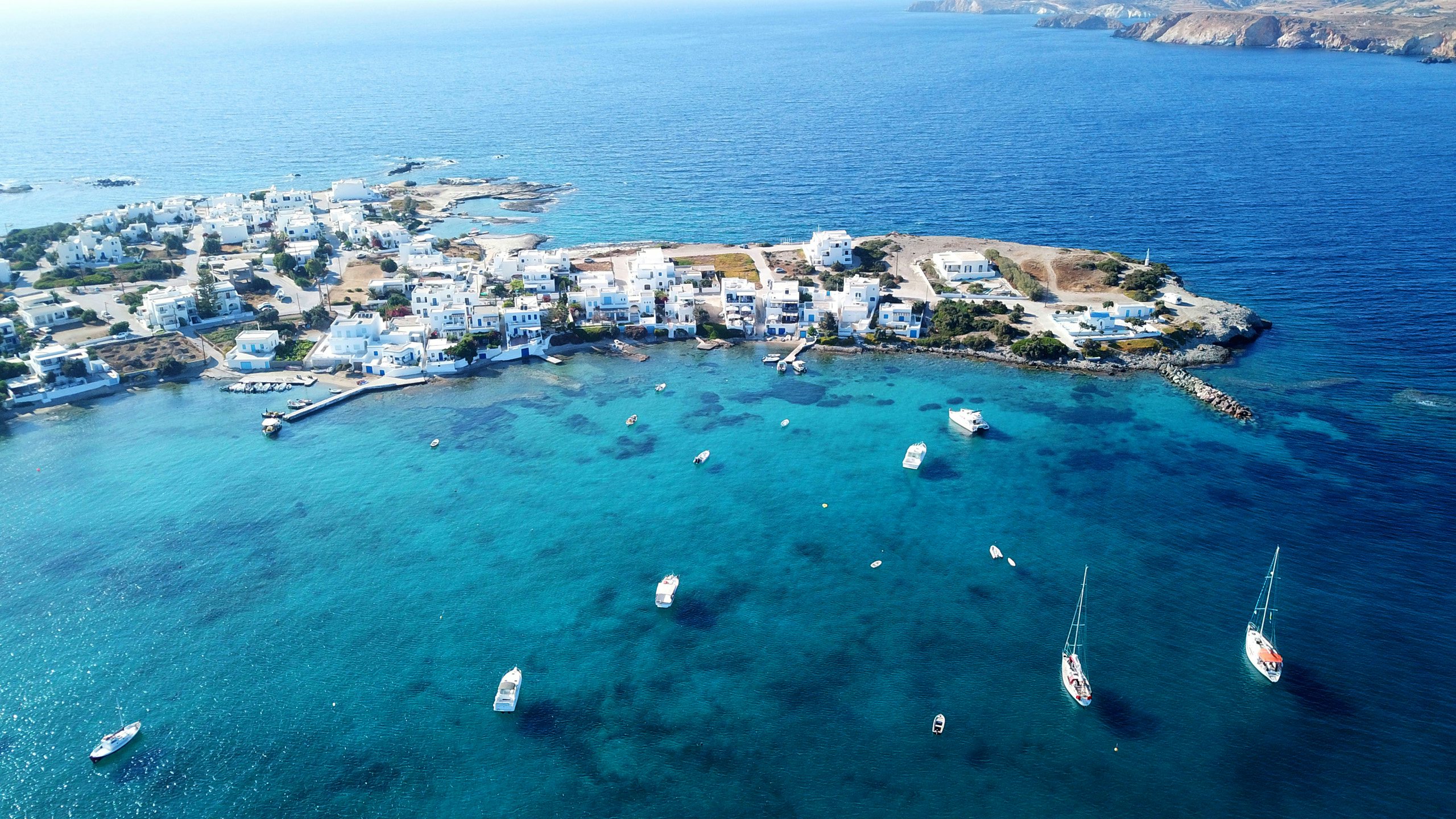 Aerial view of Milos island's crystalline waters and yachts anchored off the rocky coast, epitomizing Cyclades sailing.