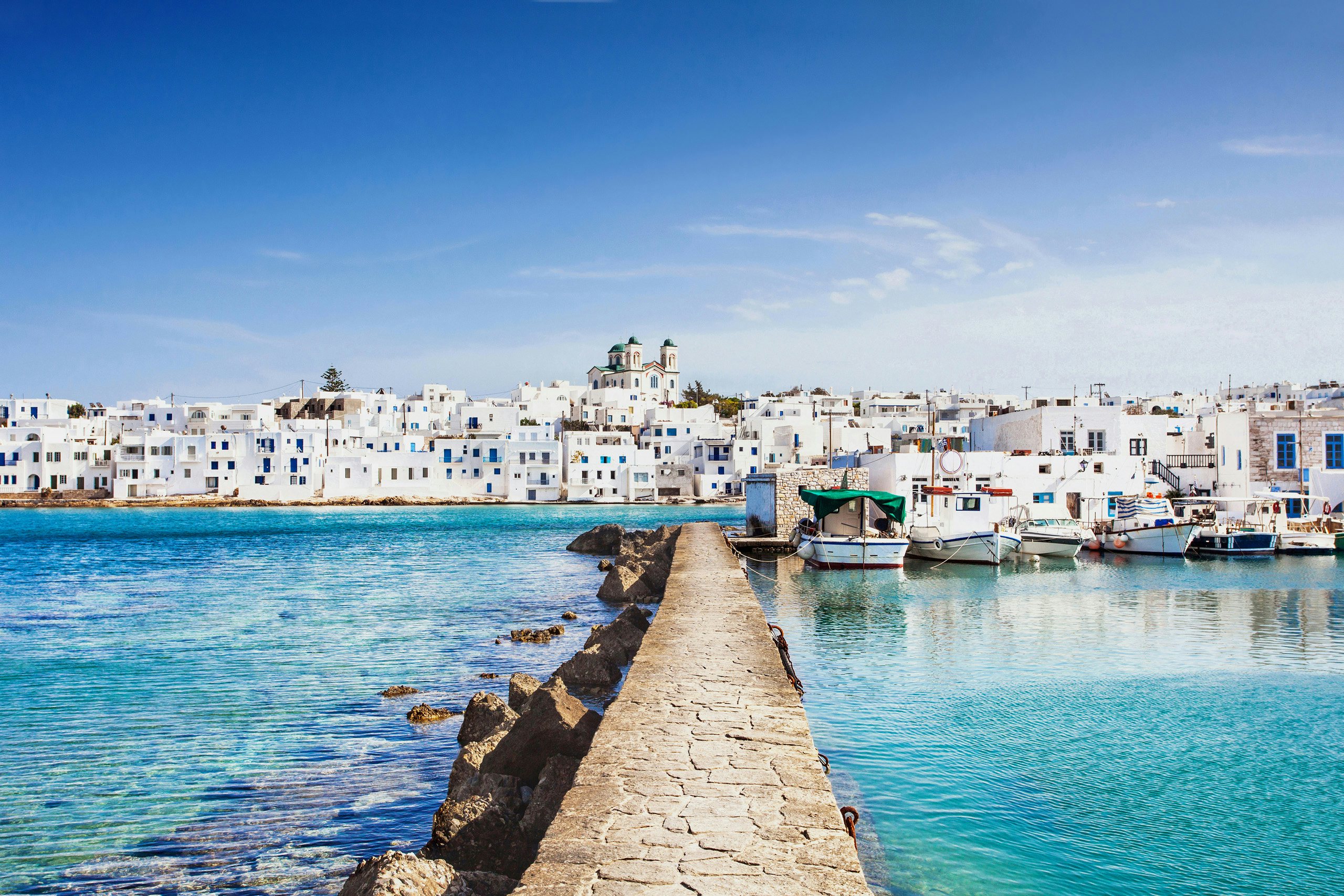 Quaint coastal town of Paros, with crystal-clear waters, viewed from a stone pier, ideal for Cyclades yacht charters