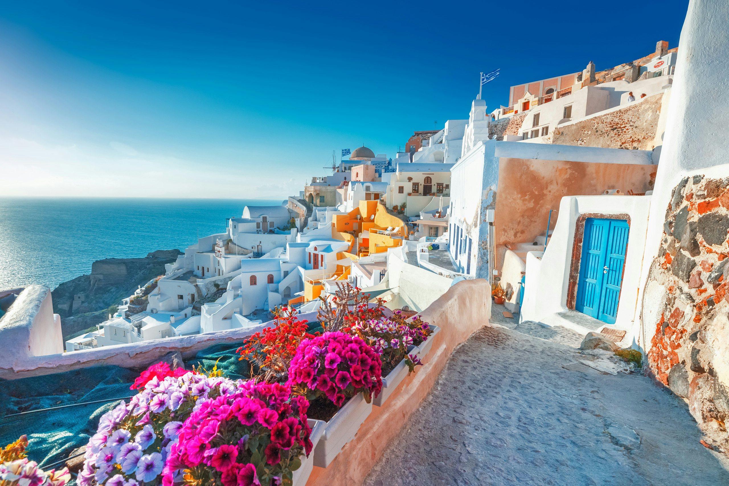 Charming Oia village in Santorini, with vibrant flowers and classic Cycladic architecture, a prime yacht charter stop.