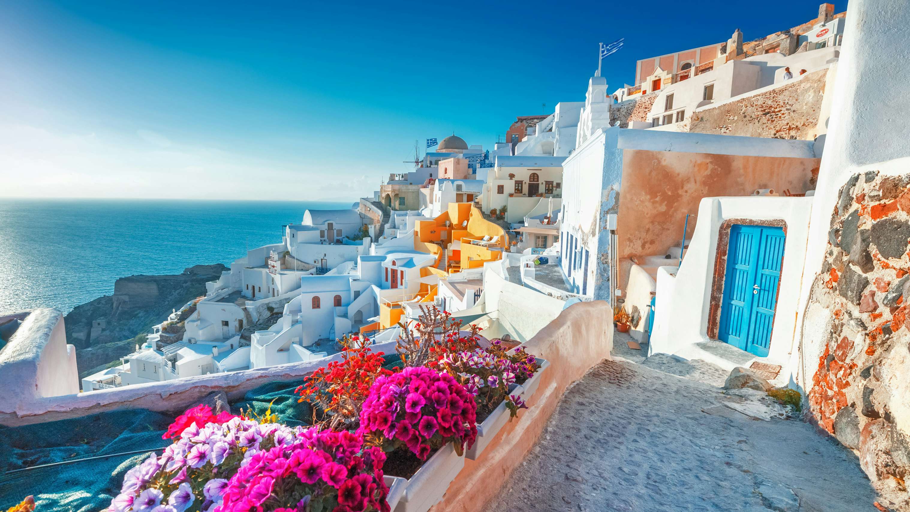 Charming Oia village in Santorini, with vibrant flowers and classic Cycladic architecture, a prime yacht charter stop.