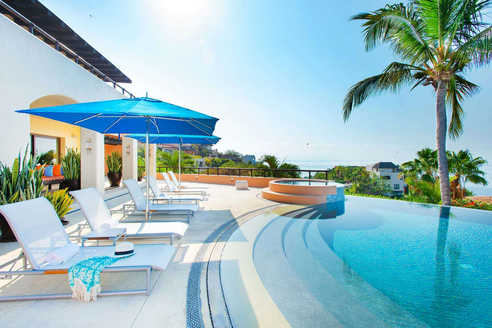 Exclusive Resorts beach villa private and exclusive vacation in the tropics umbrellas and lounge chairs by a pool with the ocean in the background