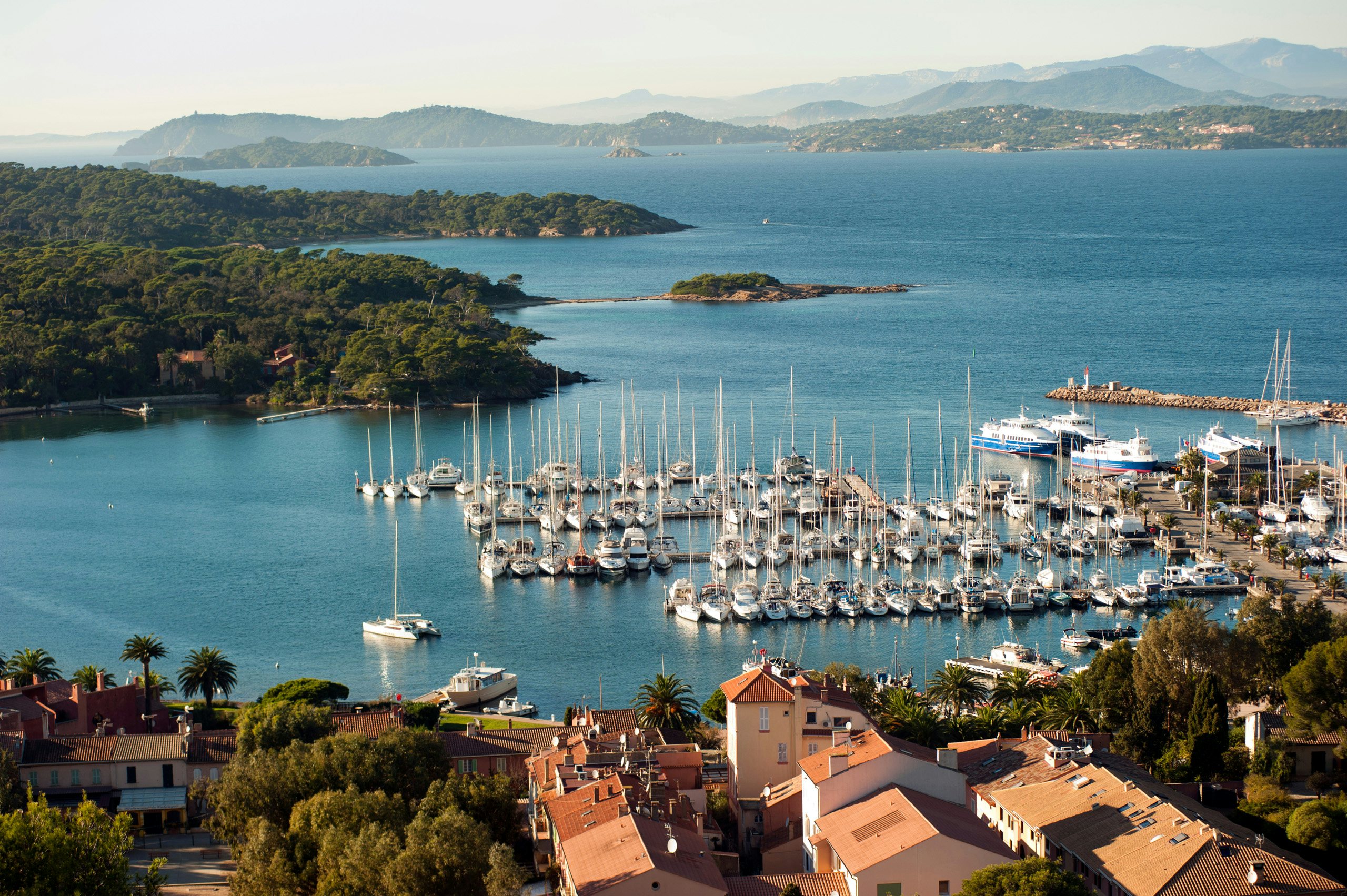 Porquerolles Island Retreat | French Riviera Yacht Charter Oasis Porquerolles Island's marina filled with yachts, surrounded by lush landscape and the expansive Mediterranean.