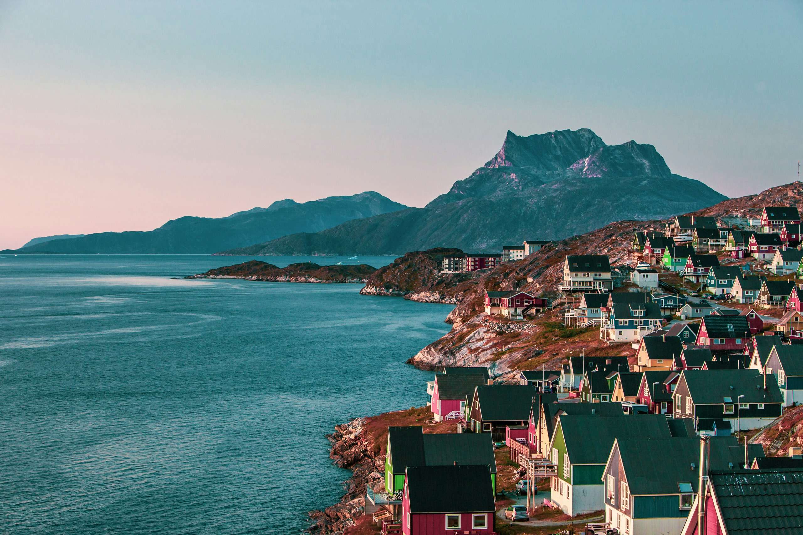 Twilight hues over a picturesque Greenlandic coastal village with colorful houses and a mountain backdrop.