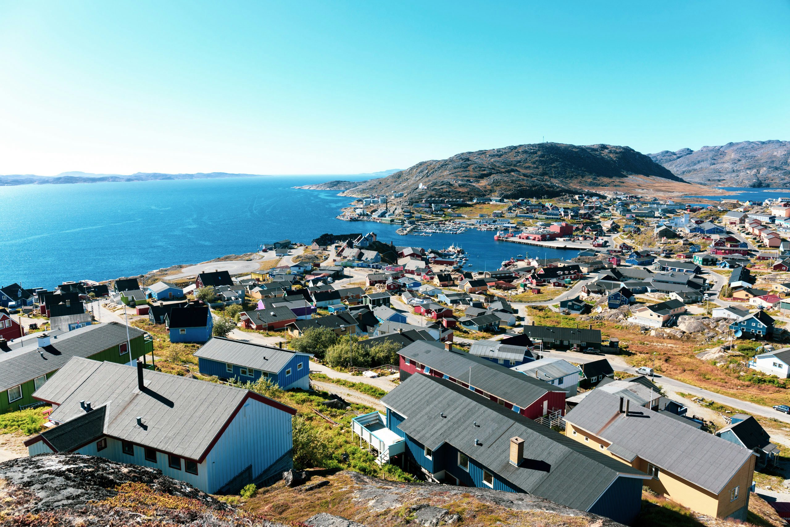 A panoramic view of a coastal Greenlandic town with colorful houses set against the backdrop of the calm sea and distant mountains.