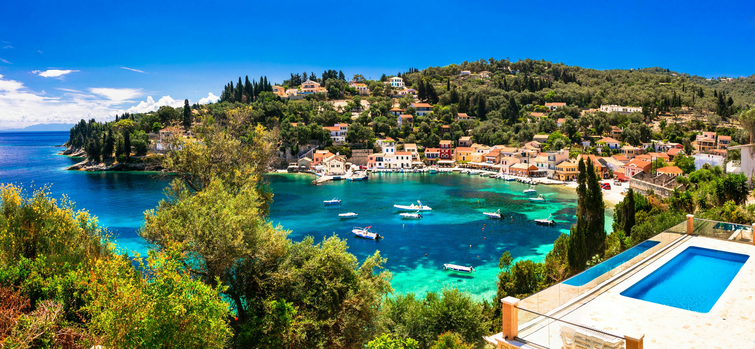 Overlooking the tranquil bay of Paxos, with yachts dotted along the clear Ionian waters, surrounded by lush greenery.