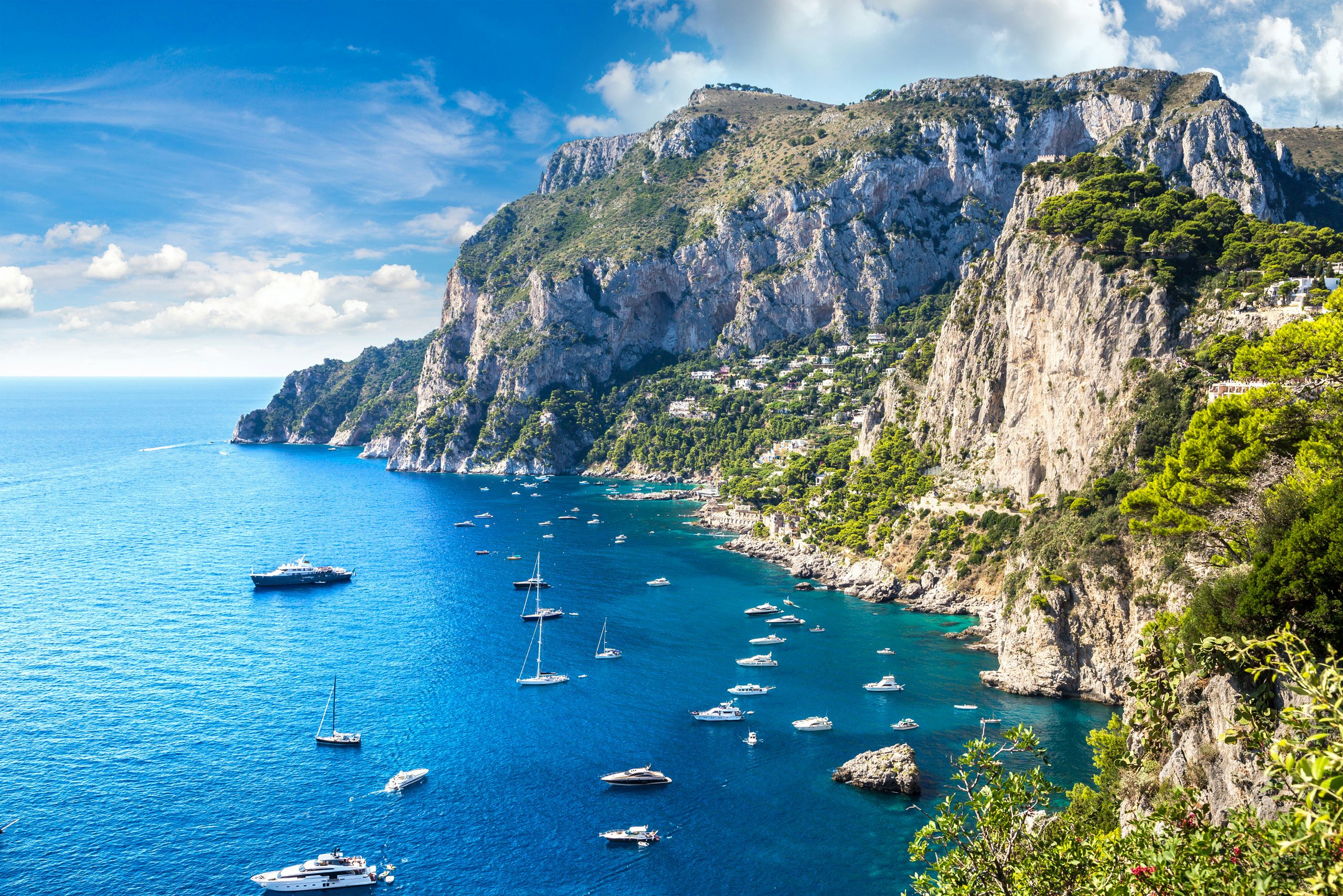 Capri Island Escape | Elite Yachting Experience | Northrop & Johnson Aerial panorama of Capri's stunning cliffs and luxury yachts sailing the Tyrrhenian Sea.