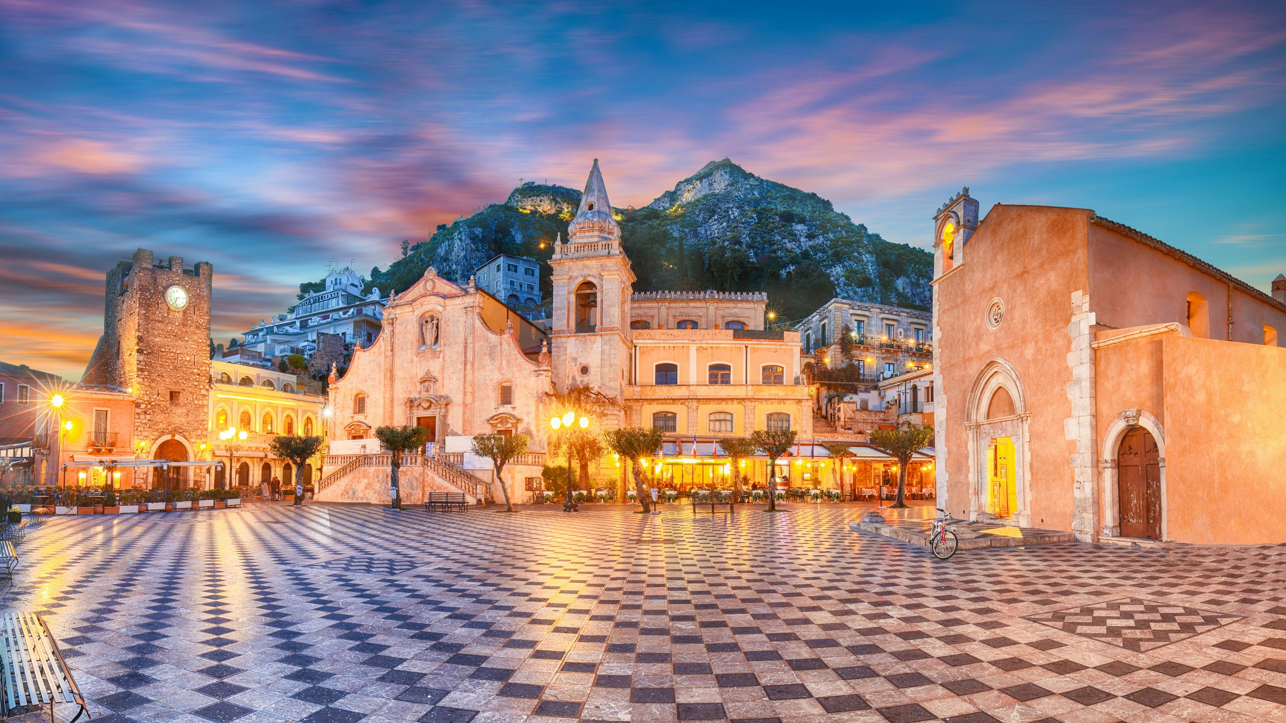 Twilight descends on a charming piazza in Sicily, with the warm glow of lights, inviting for an evening excursion from your N&J chartered yacht.