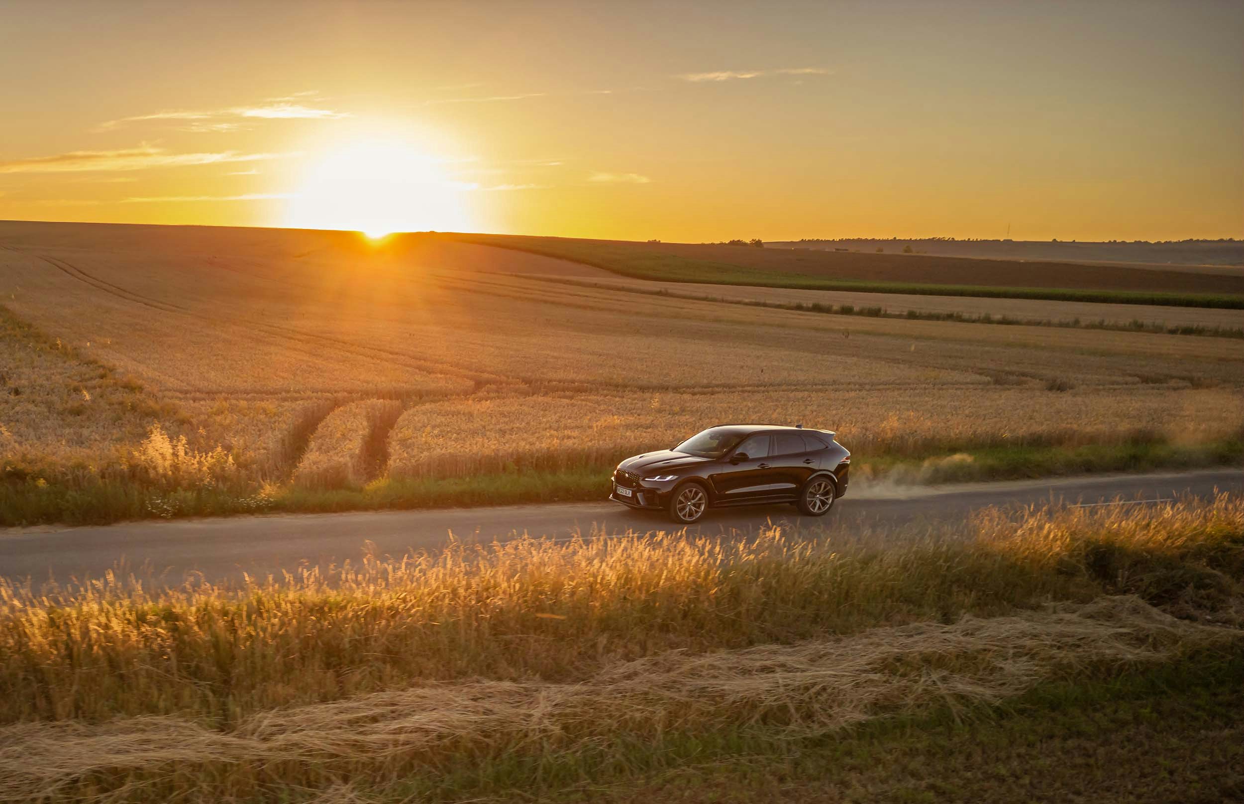 Jaguar F-Pace driving at sunset profile exterior shot of the black luxurious SUV in the countryside