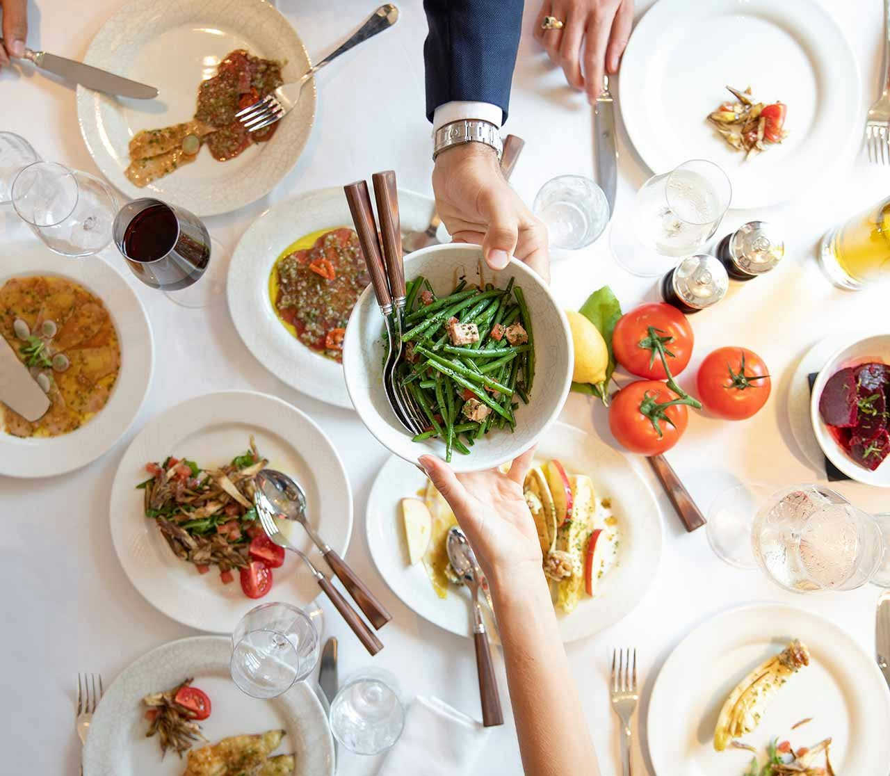 A table spread with various dishes and and a bowl of green beans being held by two hands