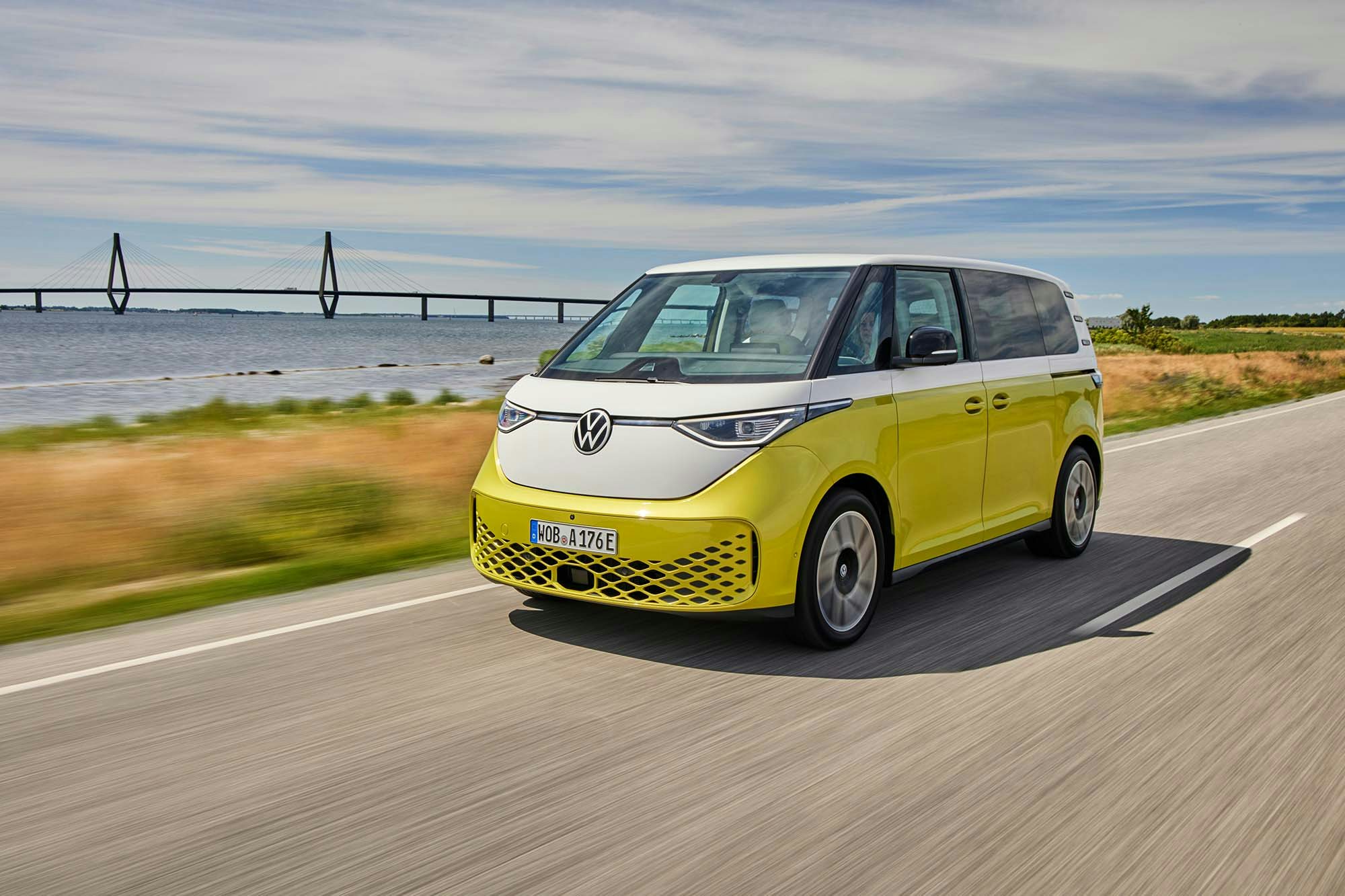 VW ID Buzz bright yellow VW van modern driving on the road with a bridge in the background