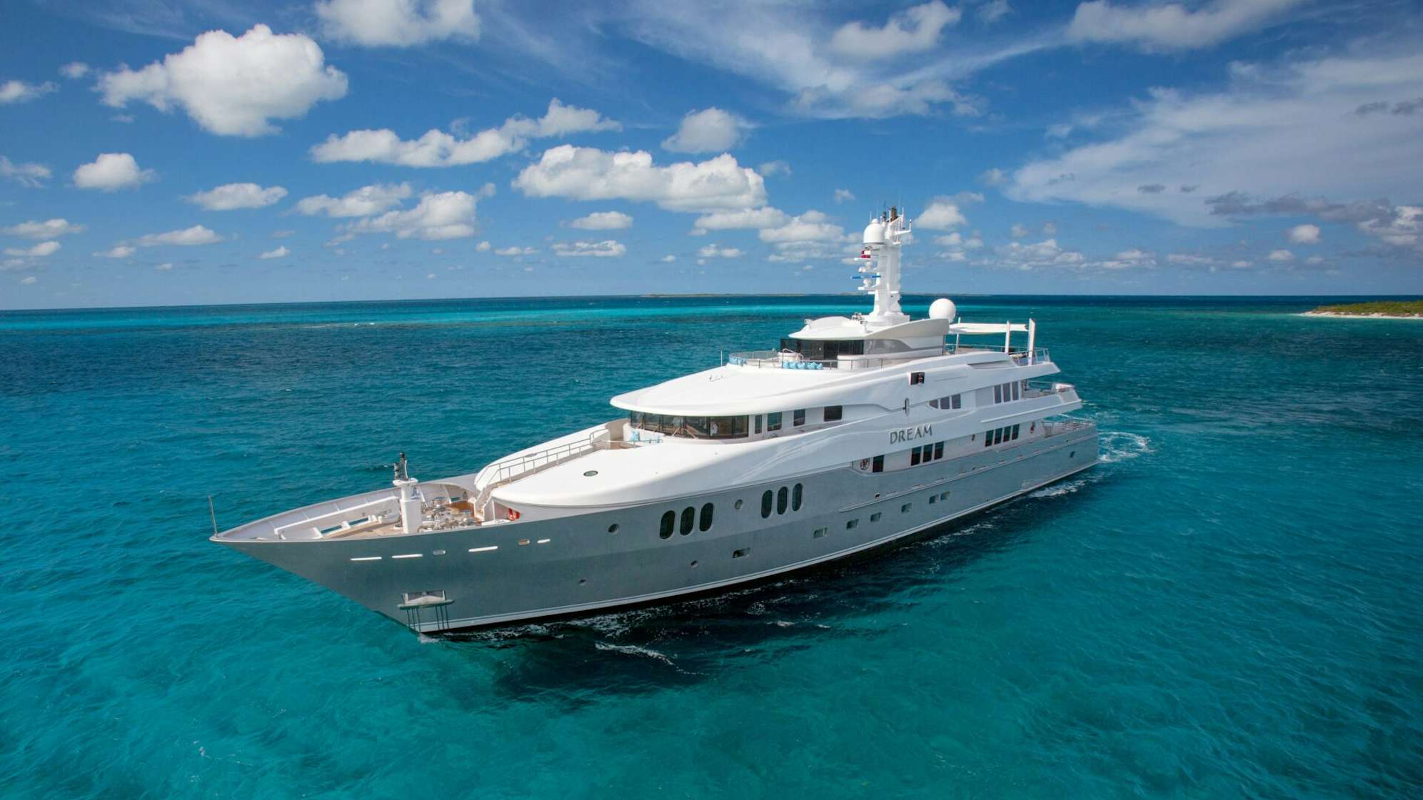 Abeking & Rasmussen luxury yacht 'DREAM' sailing near a tropical island with clear blue waters and a sunny sky.