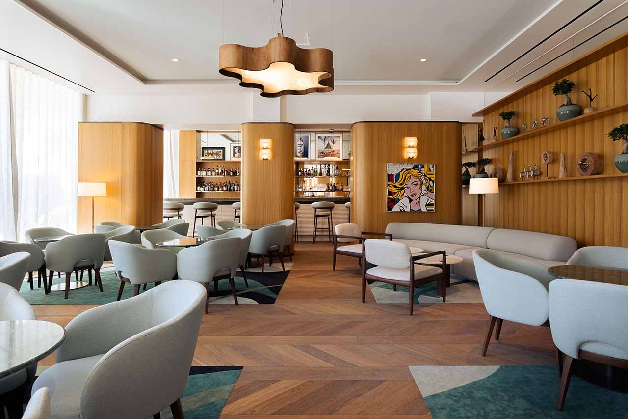 Interior of a restaurant with wood accents, grey plush armchairs around several tables