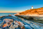 New England Yacht Charter - Lighthouse in New England with sunset ad rocky waters