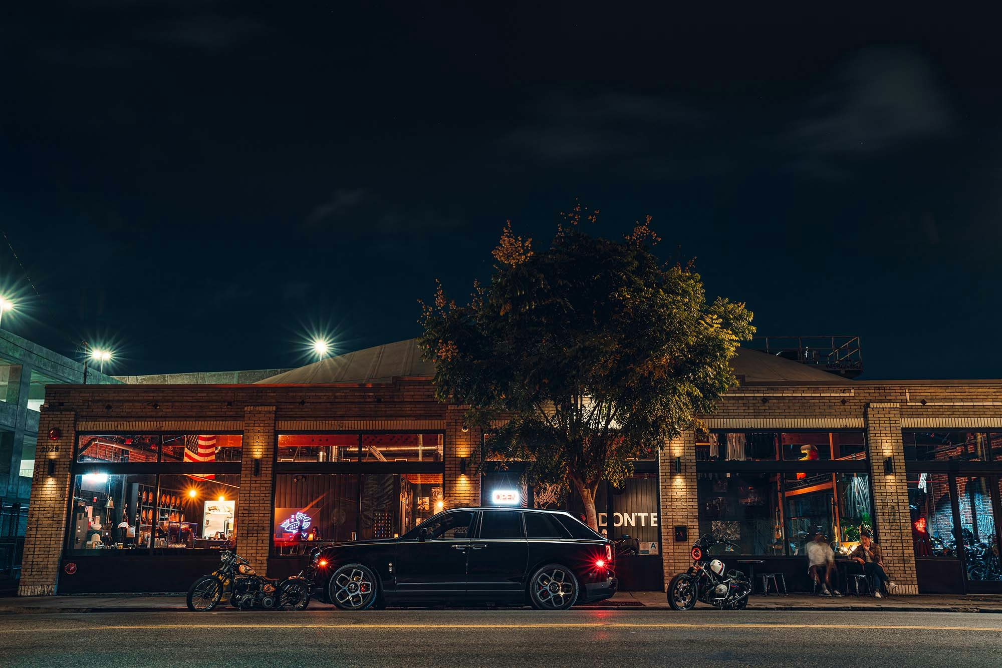 Rolls-Royce Culinan profile shot of luxury SUV at nighttime in the city with lights and the moon and a tree