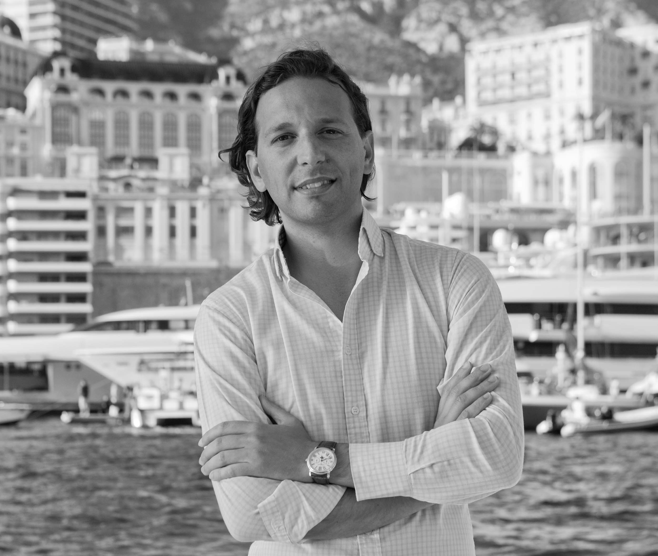 Paris Baloumis black and white with the ocean and a city as the backdrop smiling