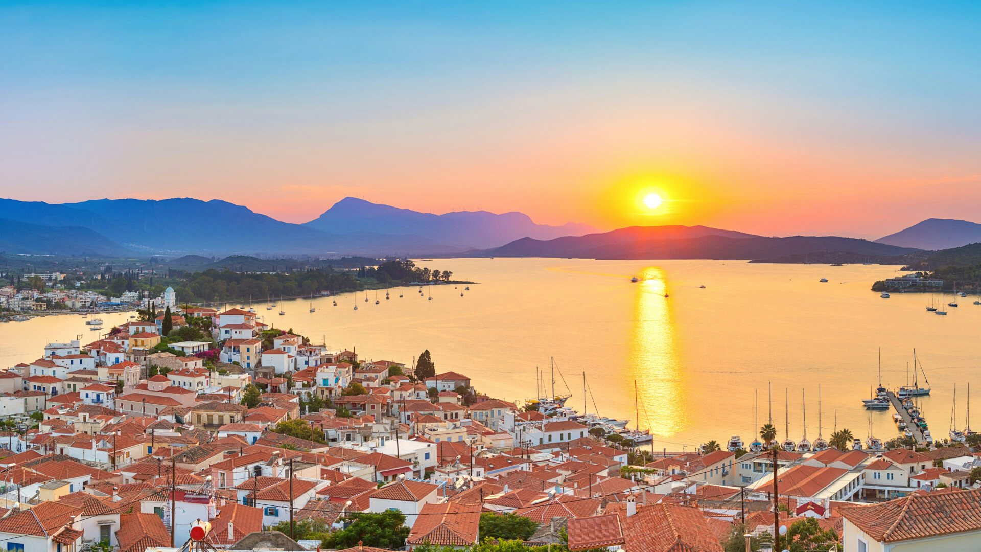 Sunset over Poros Island, with its picturesque harbor and silhouette of sailboats, a tranquil Greek yachting destination.